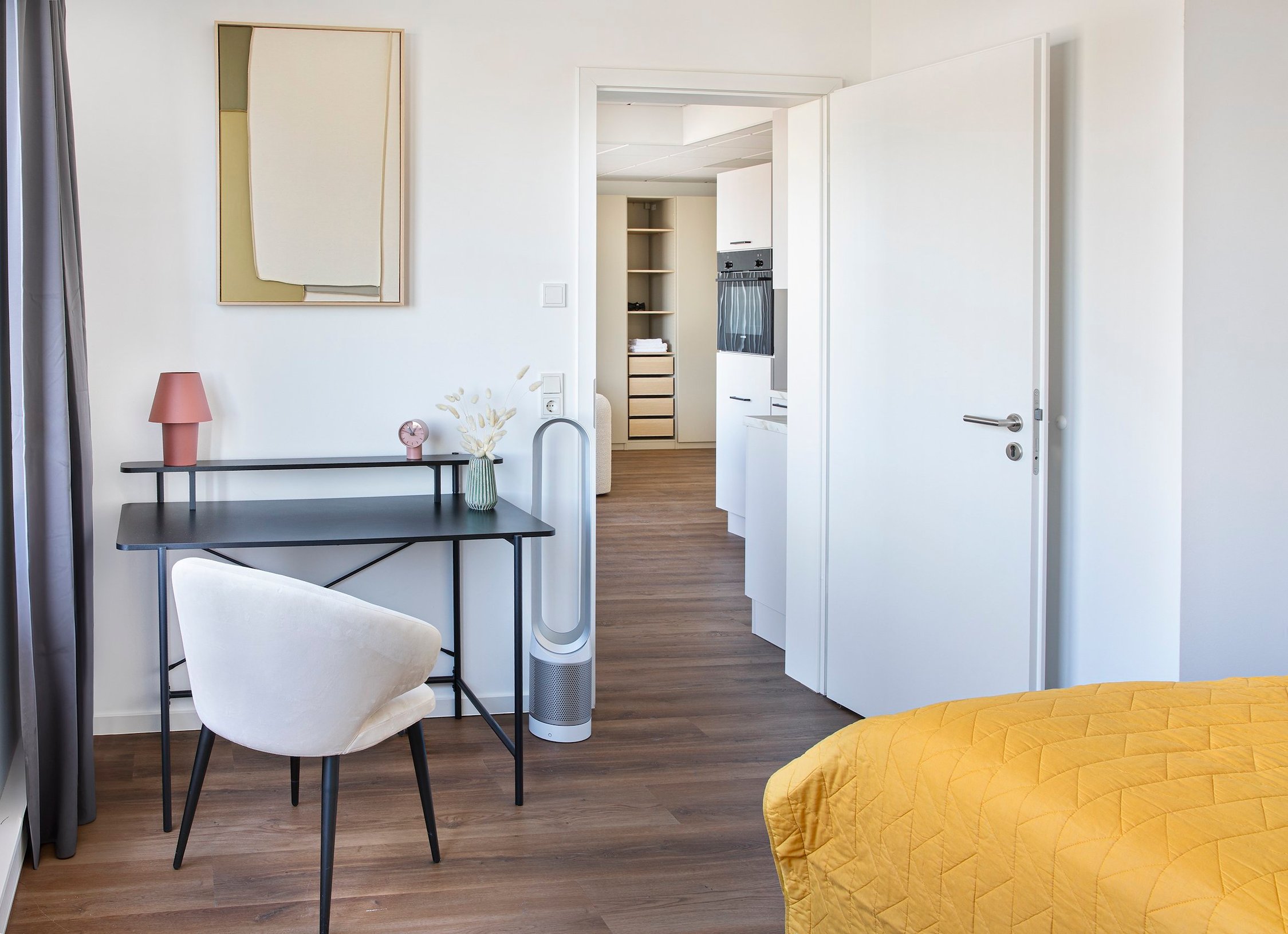 Schlafzimmer mit Schreibtisch, hellem Holzfußboden, offenem Durchgang zu Küche und Flur