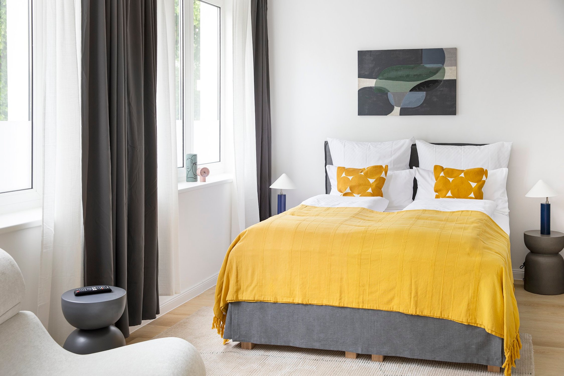 Schlafzimmer mit Doppelbett, gelbem Bettüberwurf, zwei Nachttischen und abstrakter Wandkunst