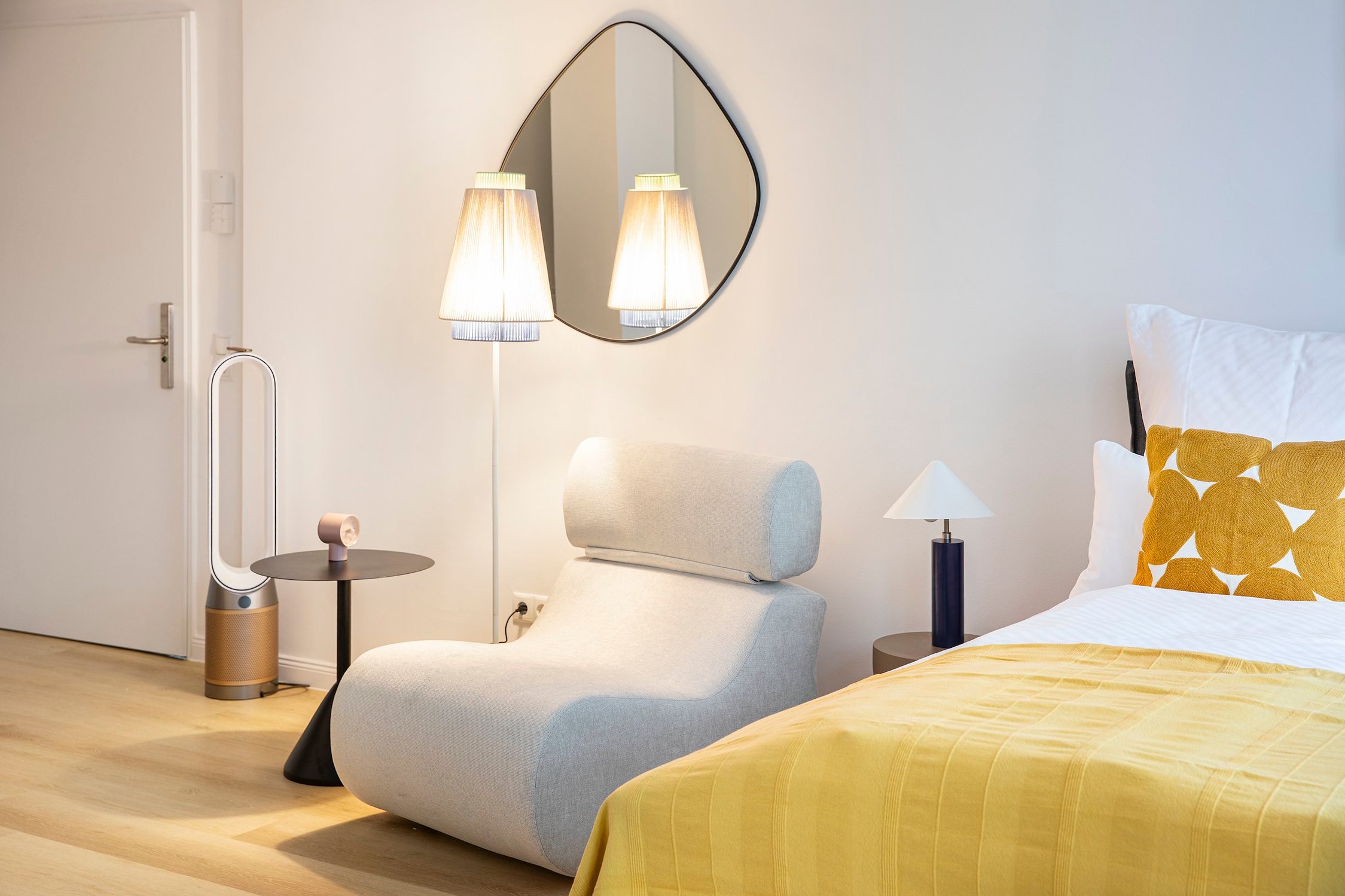 Modernes Schlafzimmer mit minimalistischem Sessel, Stehleuchte und gelbem Bettbezug