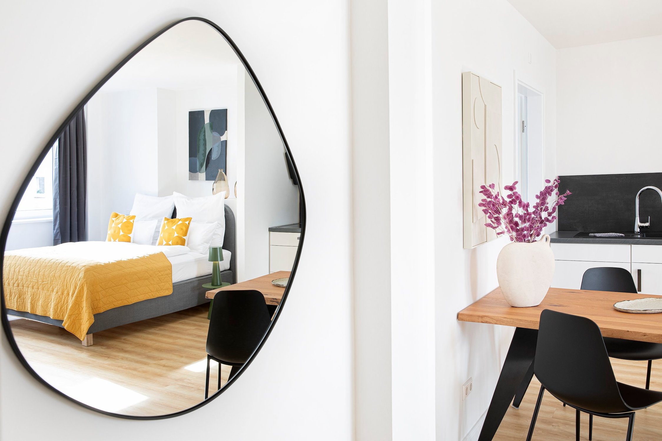 Wandspiegel mit unregelmäßigem Rand, reflektiert ein Bett mit gelber Decke und Kissen