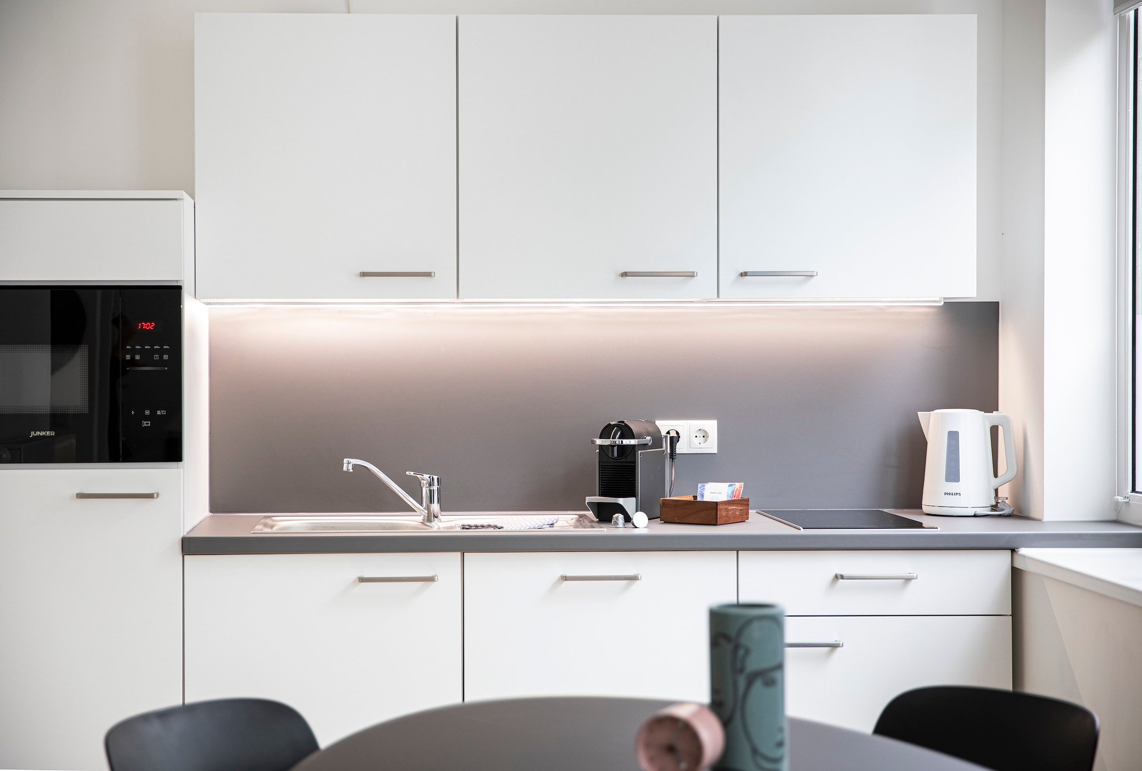 Moderne Küche mit weißen Schränken, grauem Fliesenspiegel und Arbeitsplatte, Mikrowelle, Spüle