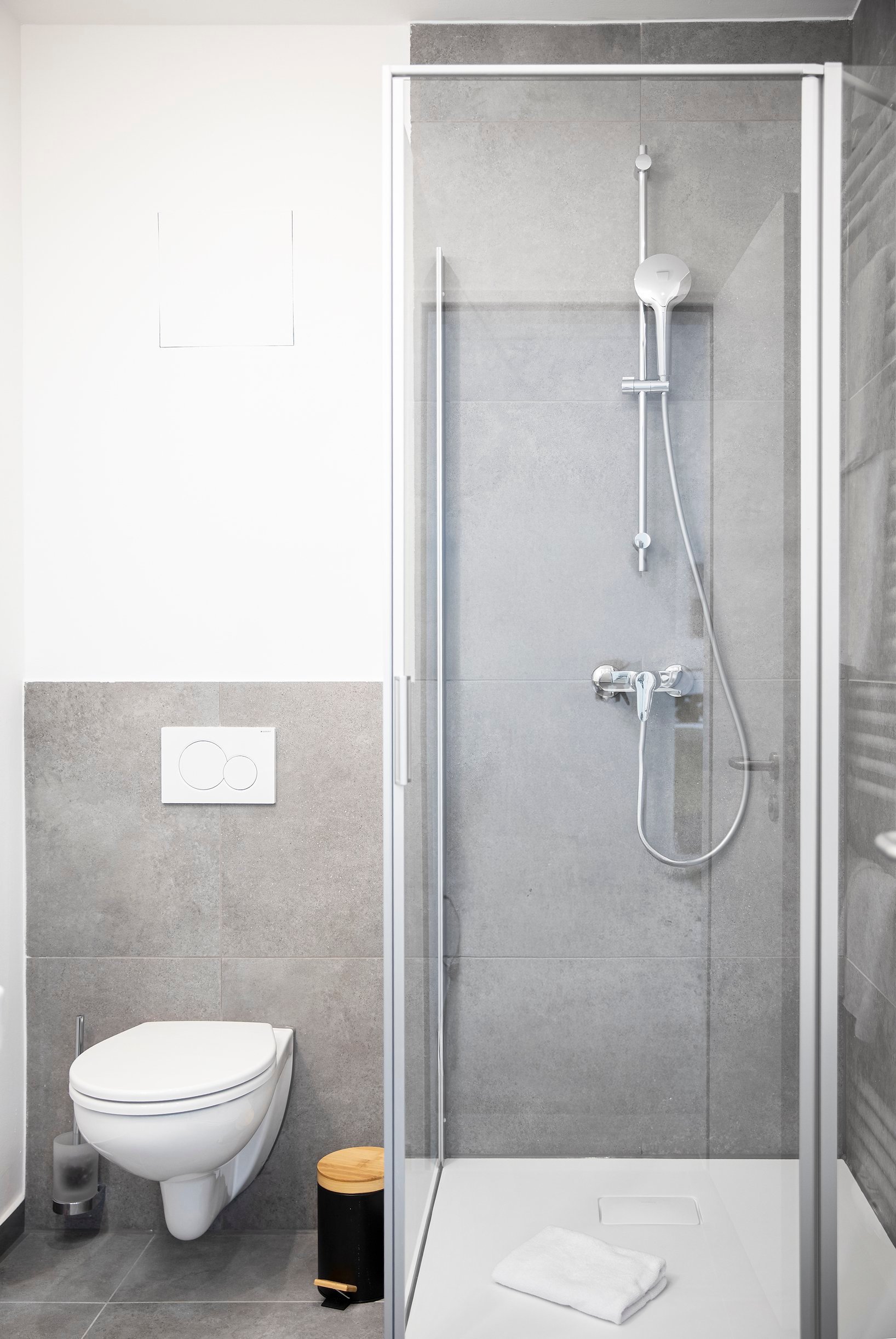 Modernes Badezimmer mit Wand-WC, grauen Fliesen und Duschkabine aus Glas mit silberner Brause