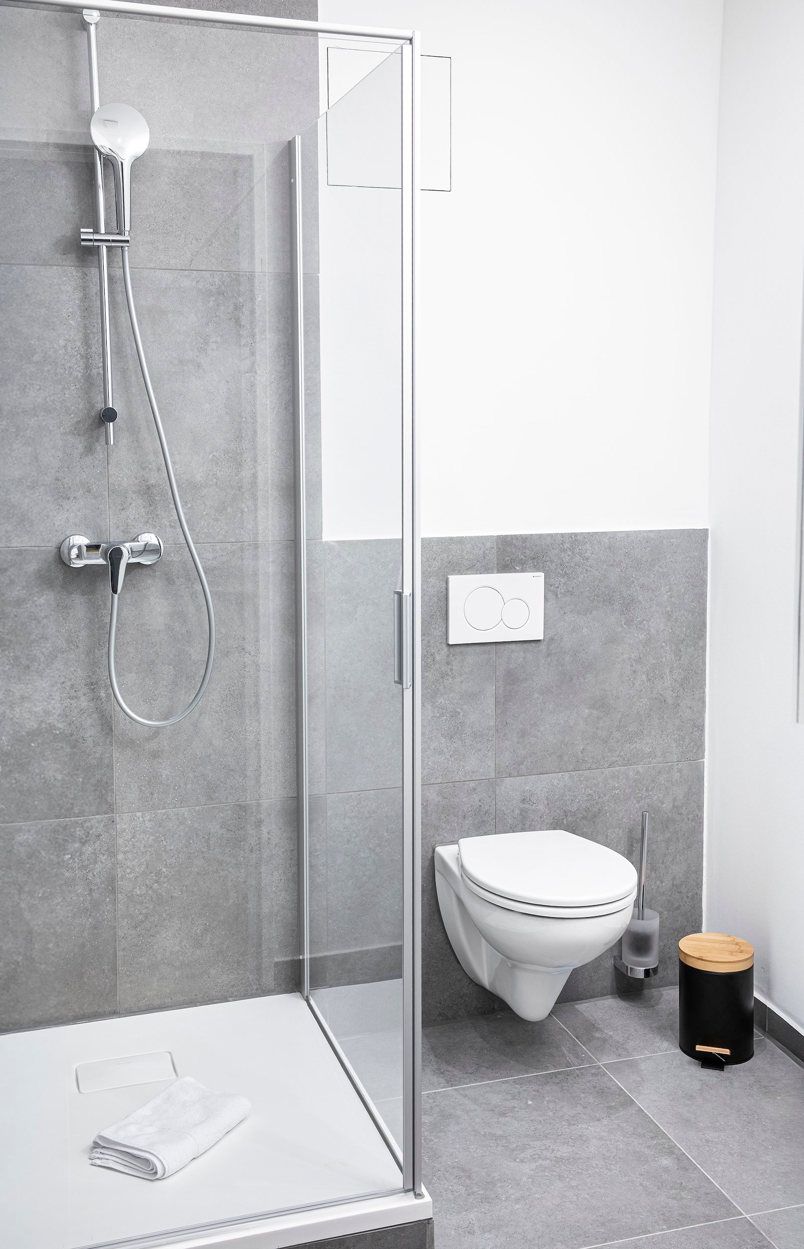 Modernes Badezimmer mit Glasdusche, weißer Toilette, grauem Fliesenboden und Wänden