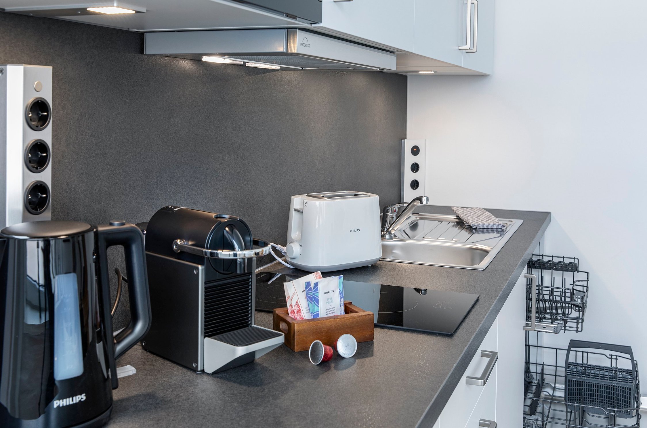 Küchenzeile mit Wasserkocher, Kaffeemaschine auf dunkler Arbeitsplatte, Spüle und Toaster