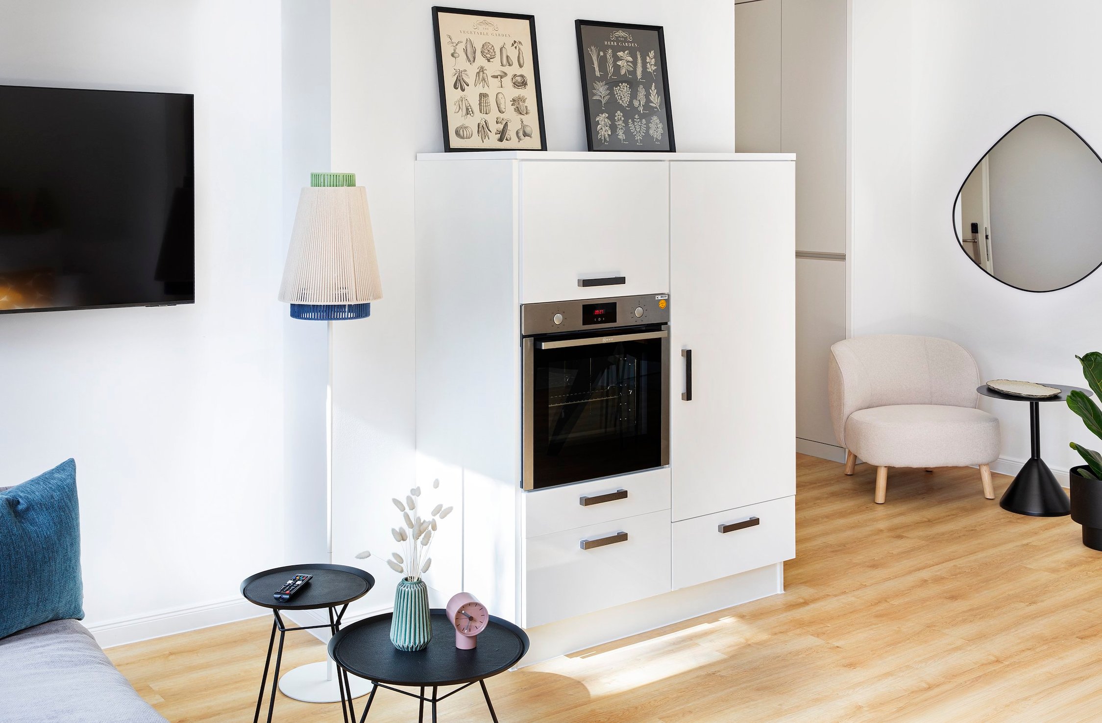 Modernes Wohnzimmer mit weißer Küchenzeile, hellem Holzboden und dekorativer Stehleuchte