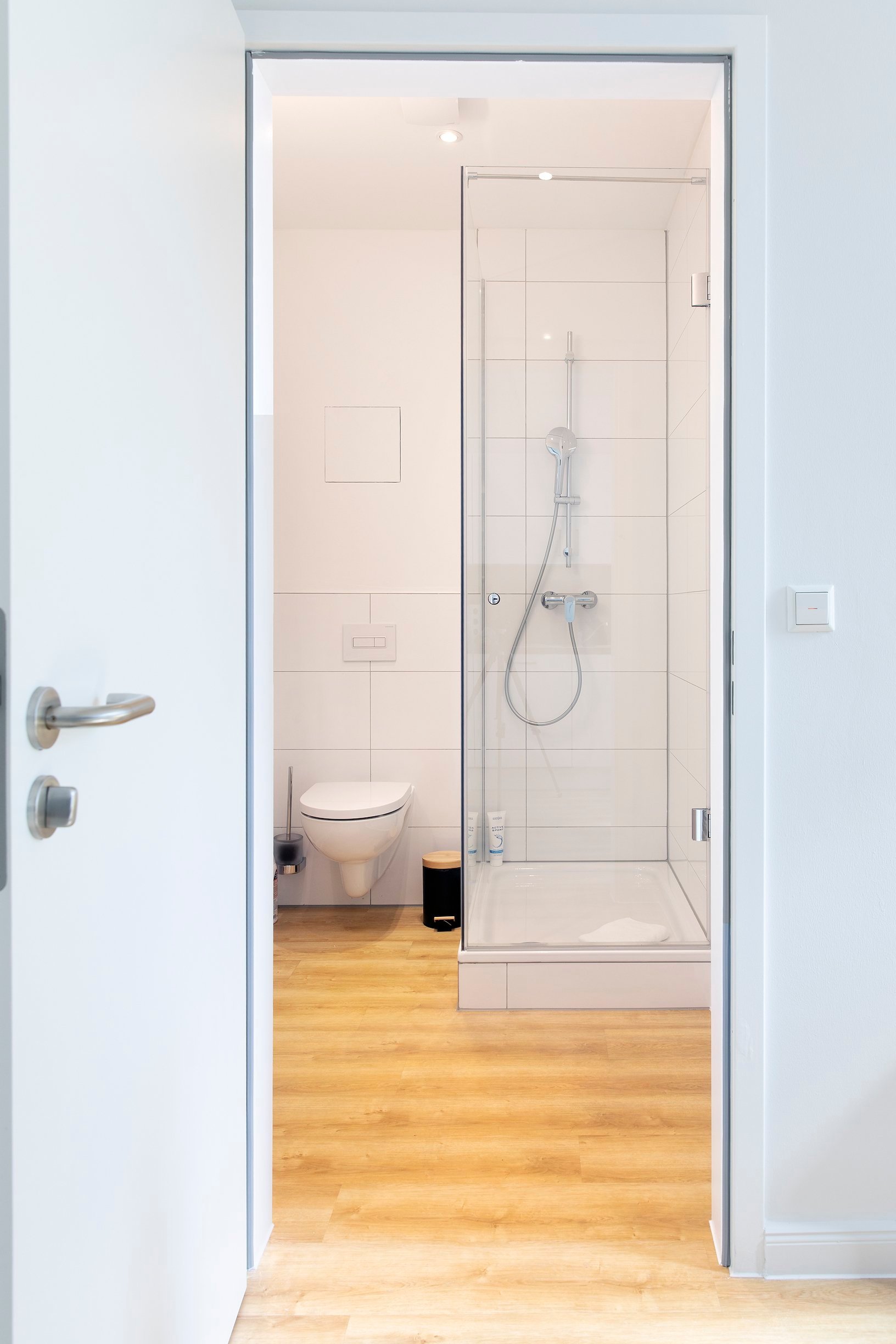 Badezimmer mit heller Holzbodenoptik, weißer Toilette und Duschkabine, sauber