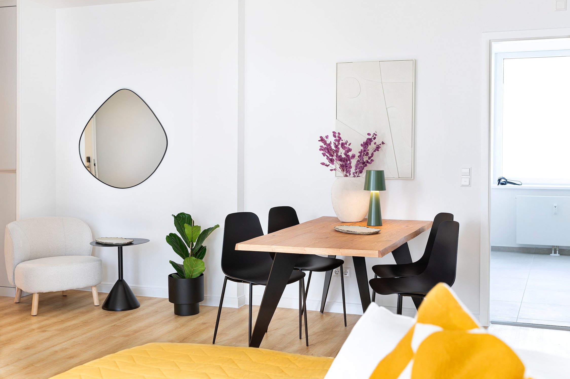 Esszimmer mit Holztisch für vier Personen, schwarze Stühle, beiger Sessel, Spiegel, Pflanze, Vase