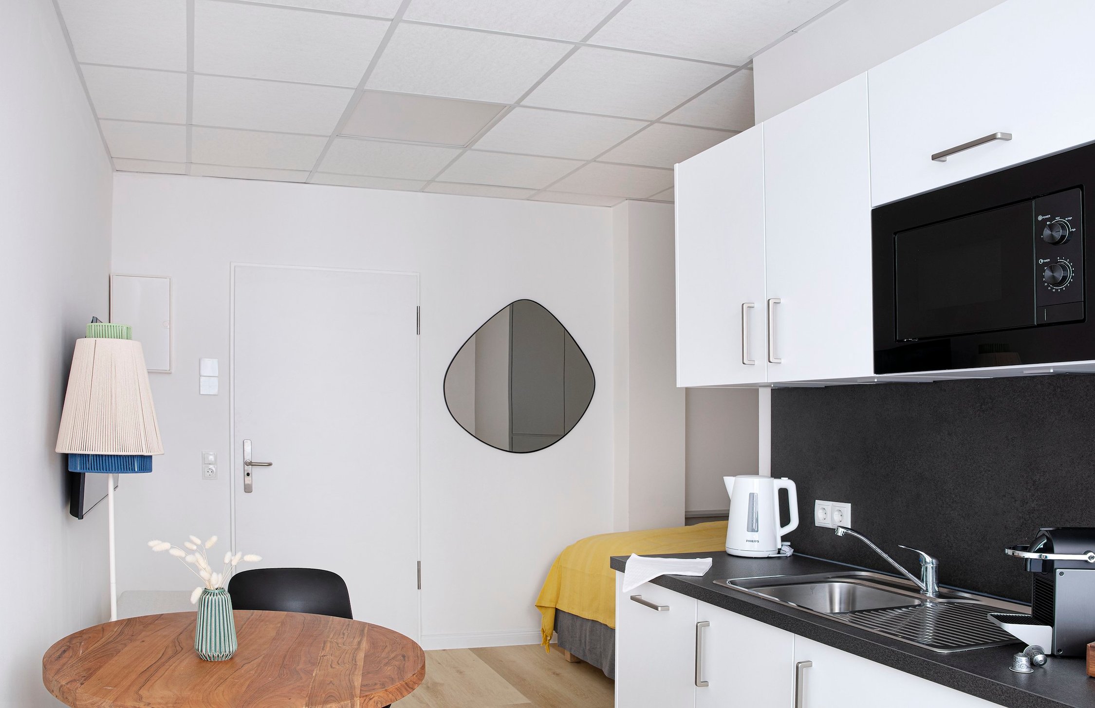 Helles Einraumappartement mit Holztisch und Miniküche, Schrankbett, weißer Decke