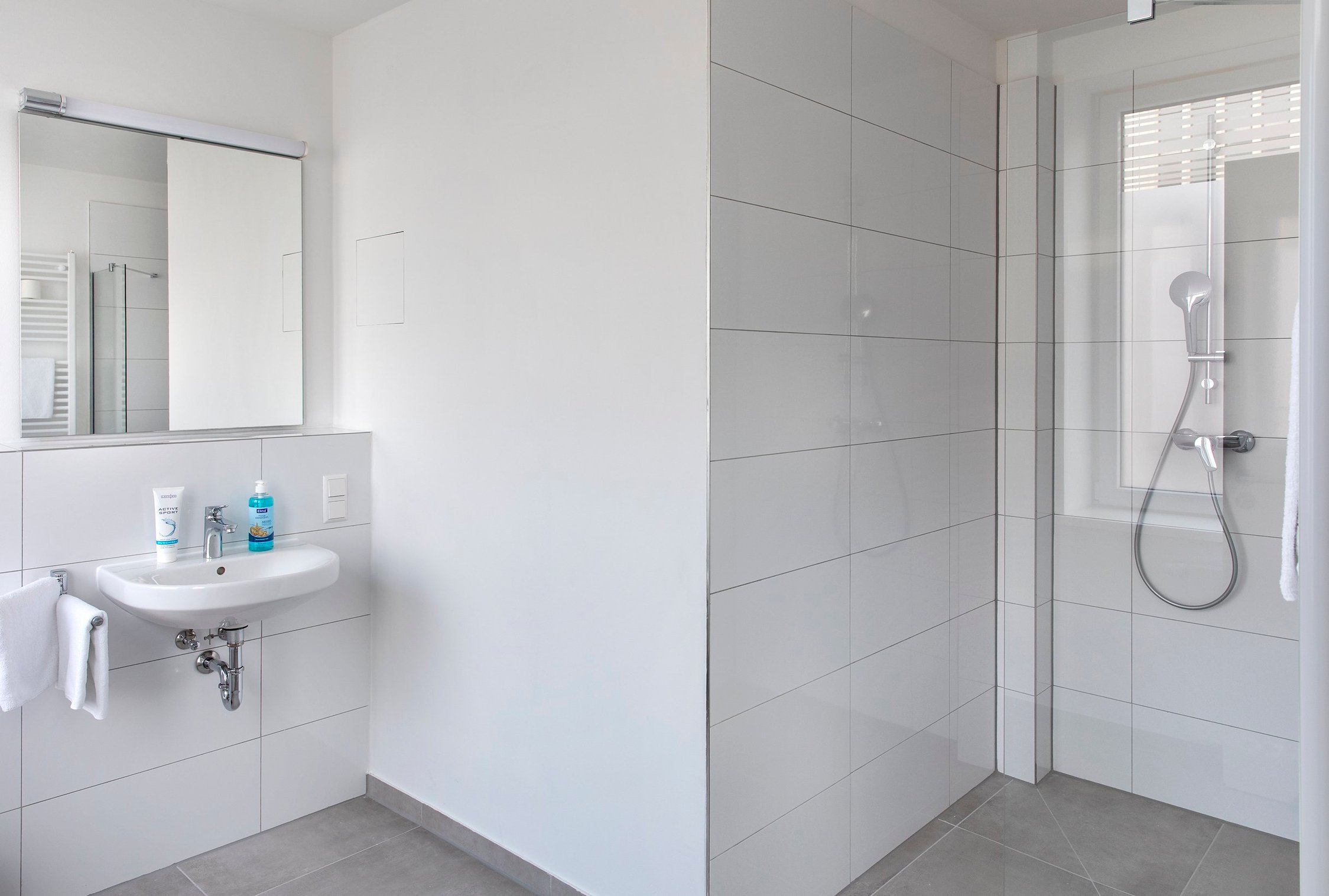 Helles Badezimmer mit weißem Waschbecken, Spiegelschrank, Dusche und weißen Fliesen