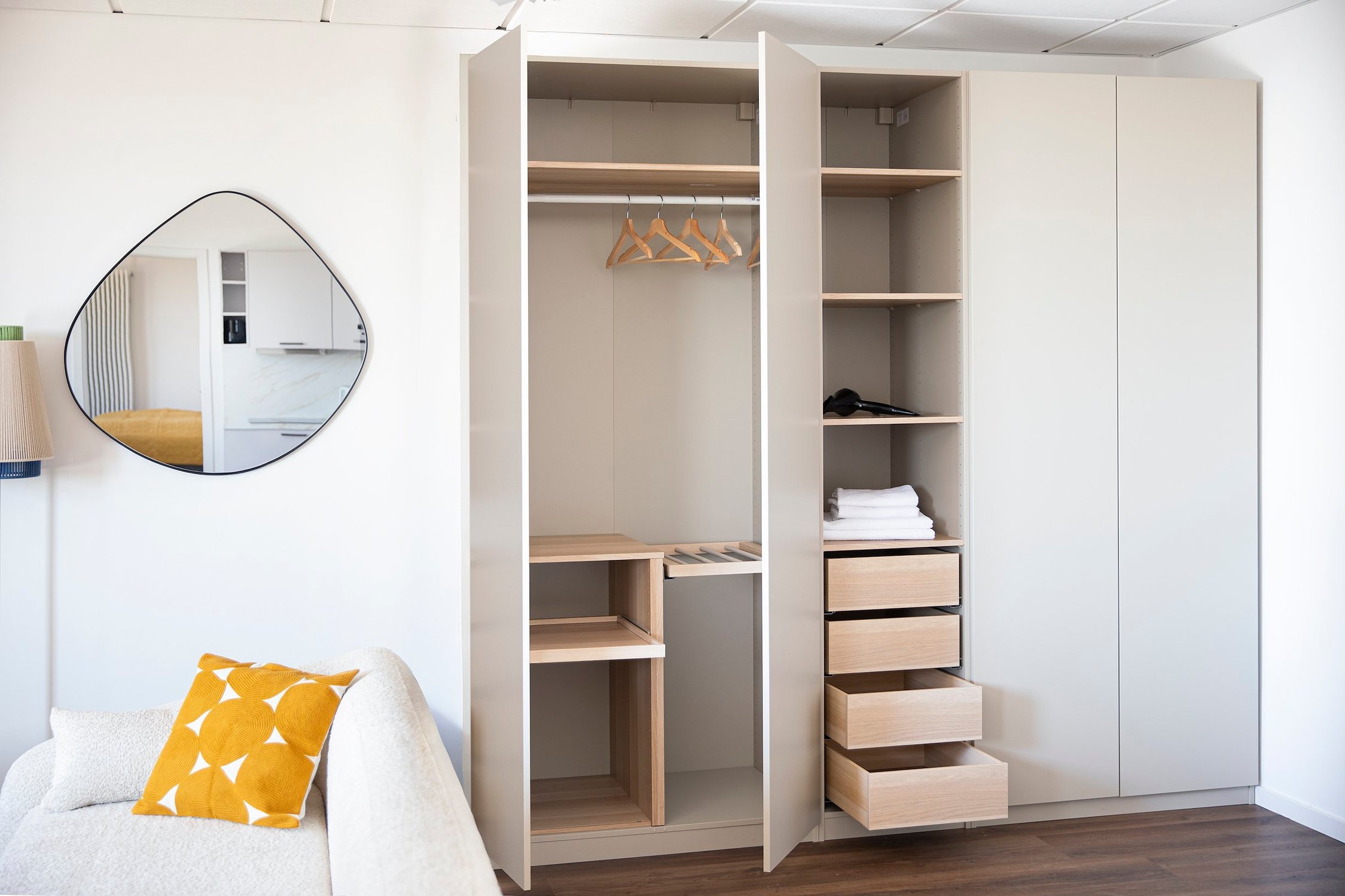 Offener Kleiderschrank in Weiß mit Holzschubladen, Spiegel und weißem Sofa mit Kissen