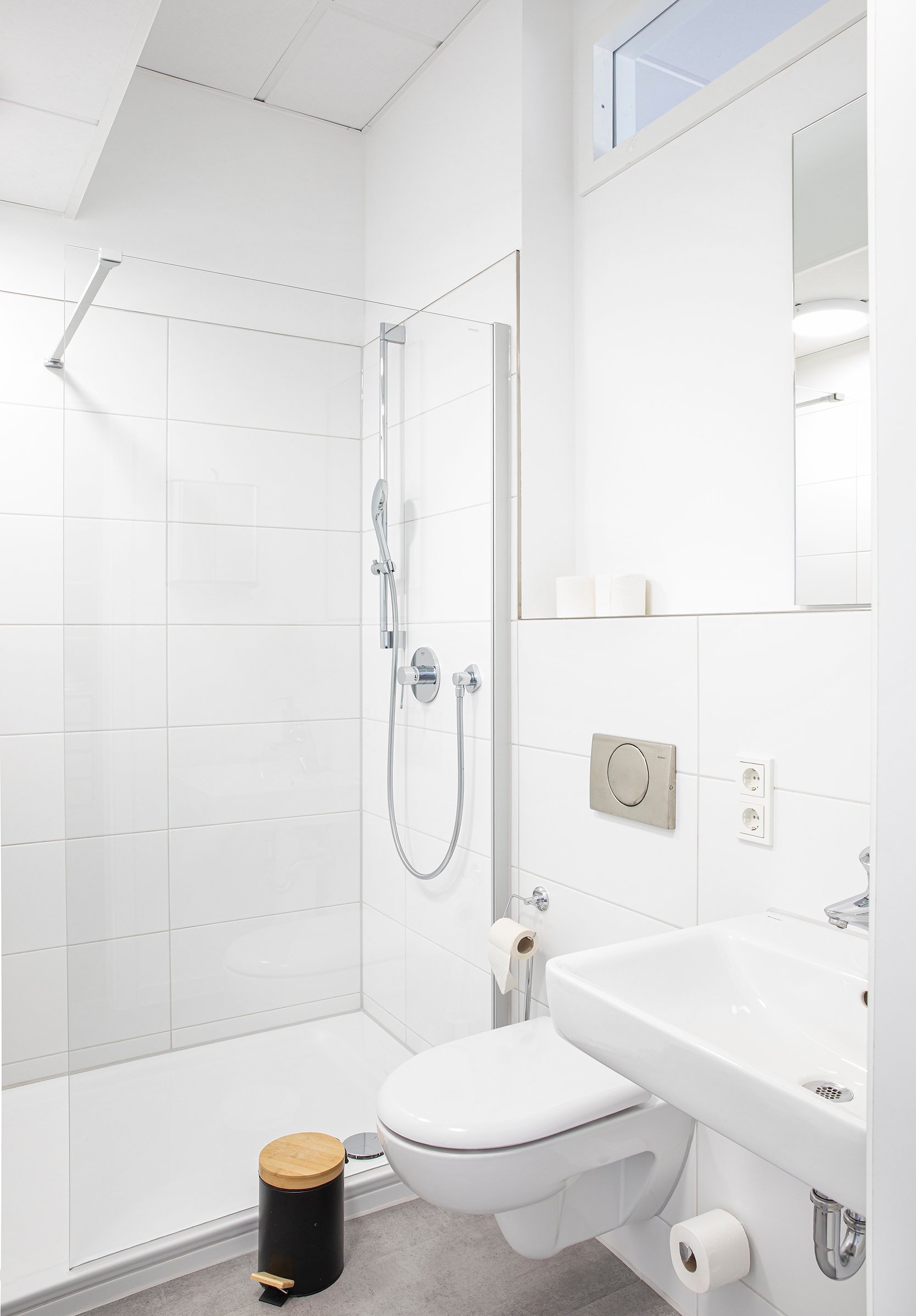 Helles Badezimmer mit weißen Fliesen, gläserner Duschkabine, Toilette und Waschbecken
