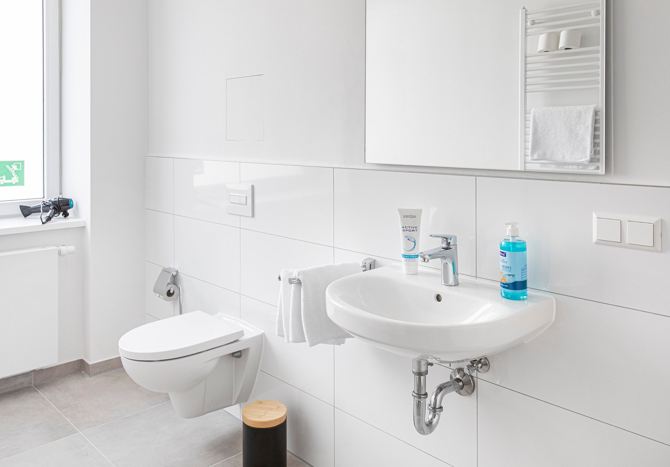 Modernes weißes Badezimmer mit Waschbecken, Toilette, Spiegel und Handtuchheizkörper, helle Fliesen