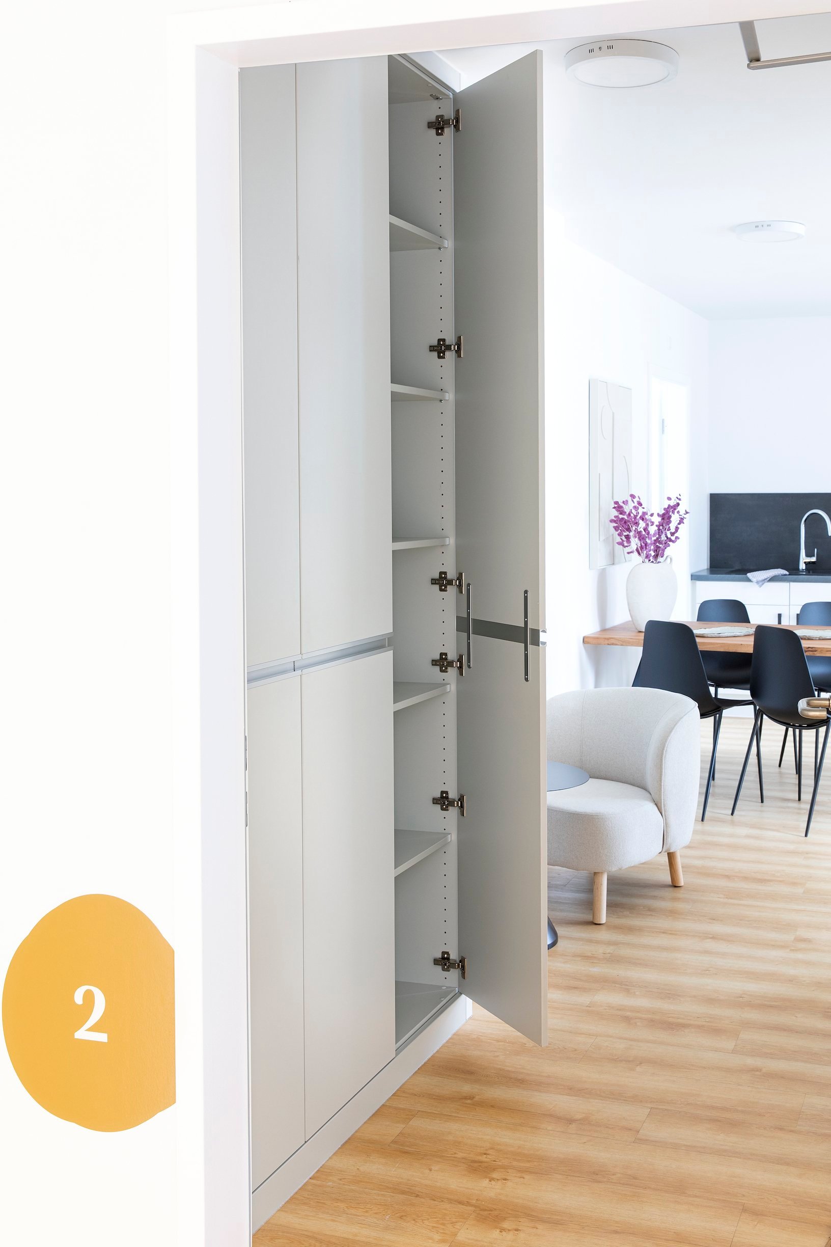 Hoher weißer Schrank mit geöffneter Tür, Regalbrettern im Inneren, heller Holzfußboden