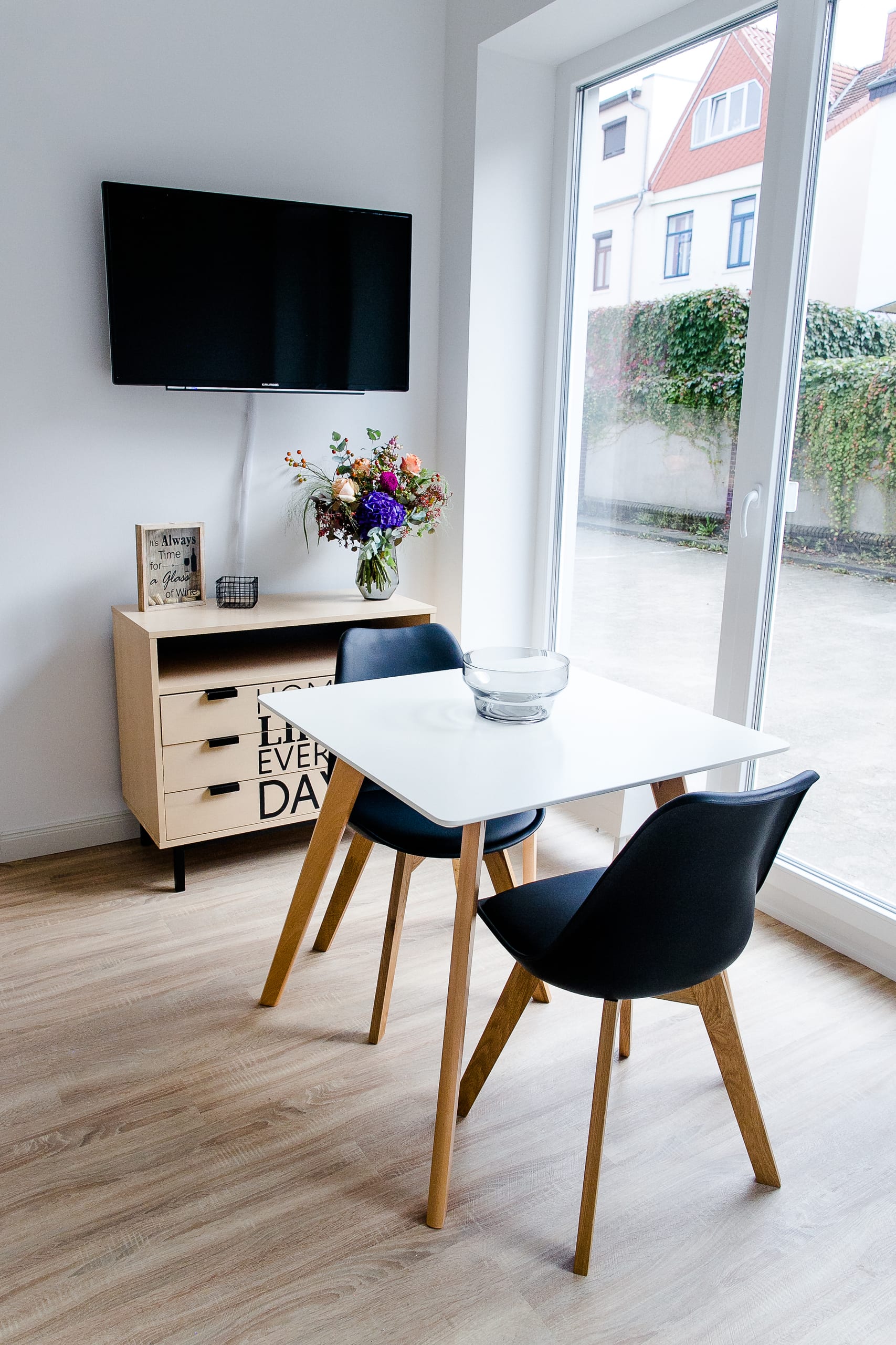 Heller Raum mit Esstisch und zwei Stühlen in Schwarz und Holz, an Fensterfront