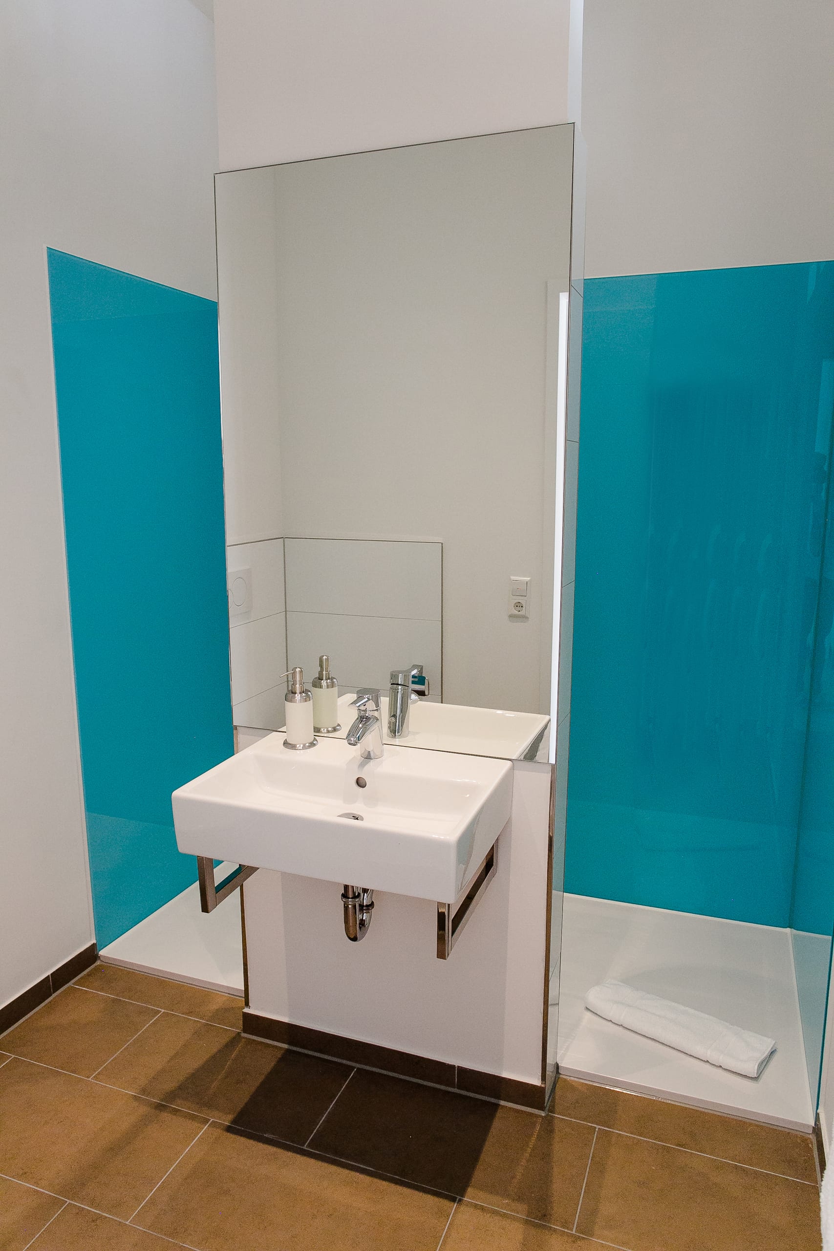 Modernes Badezimmer mit weißem Waschbecken, großem Spiegel und blauen Akzentwänden, Holzfliesen