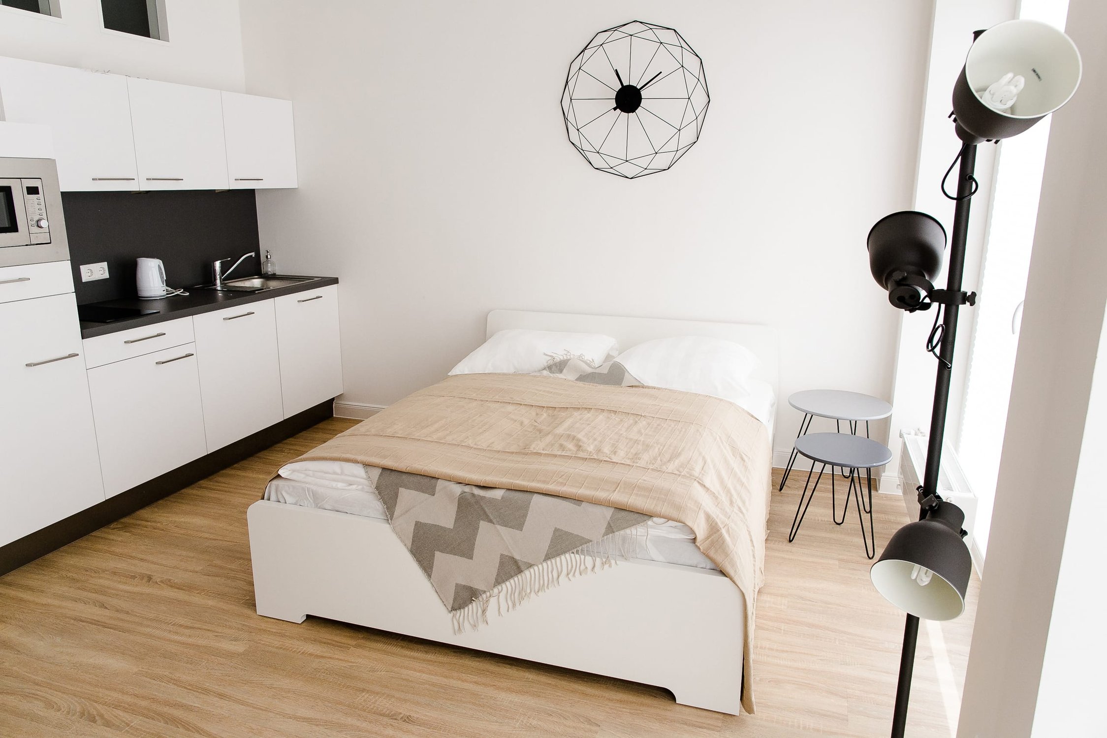 Modernes Studio-Apartment mit Küchenzeile, Bett, zwei Beistelltischen und Stehlampe