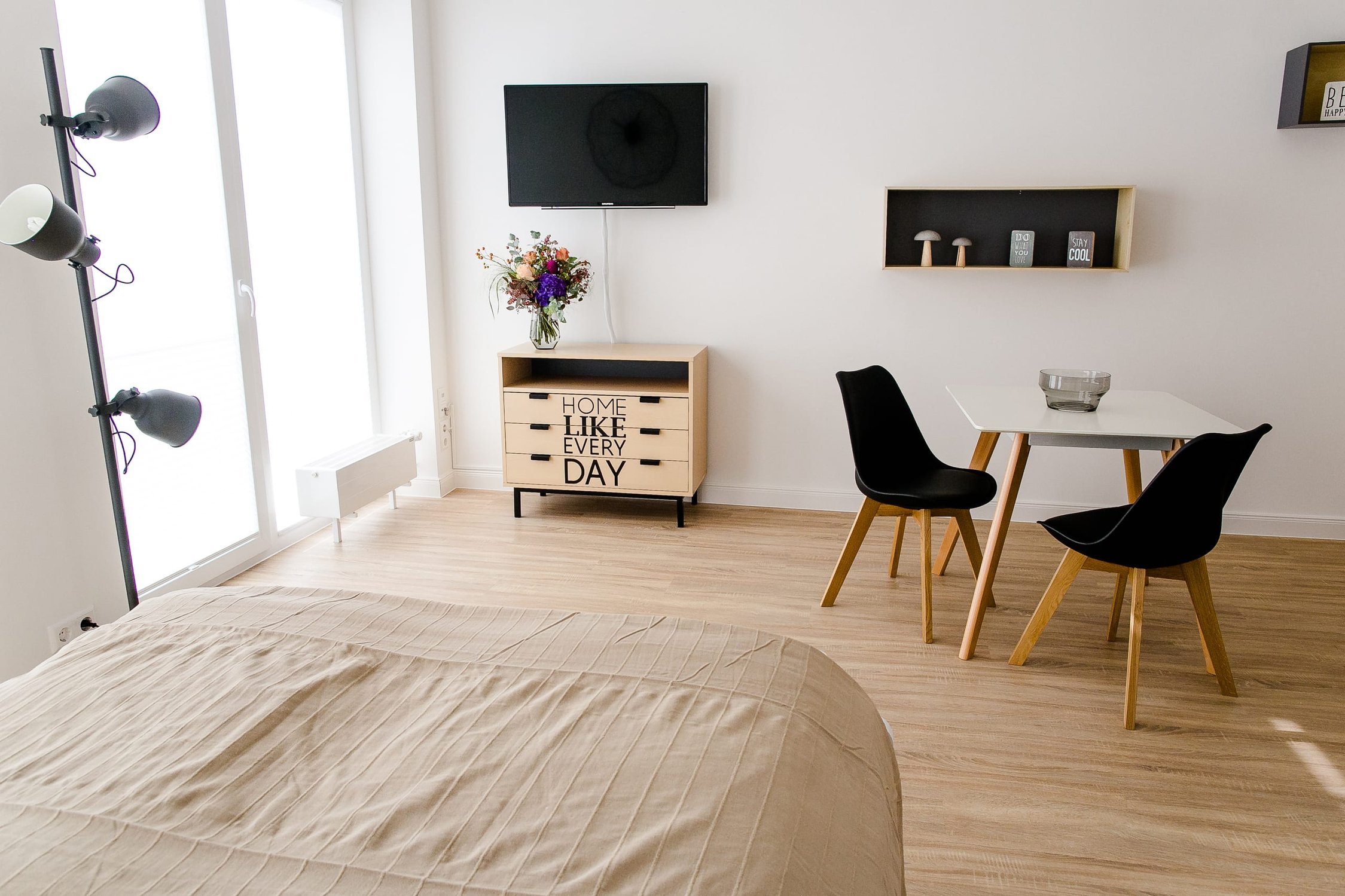 Helles Schlafzimmer mit Holzboden, großem Fenster, Bett und Tisch mit zwei schwarzen Stühlen