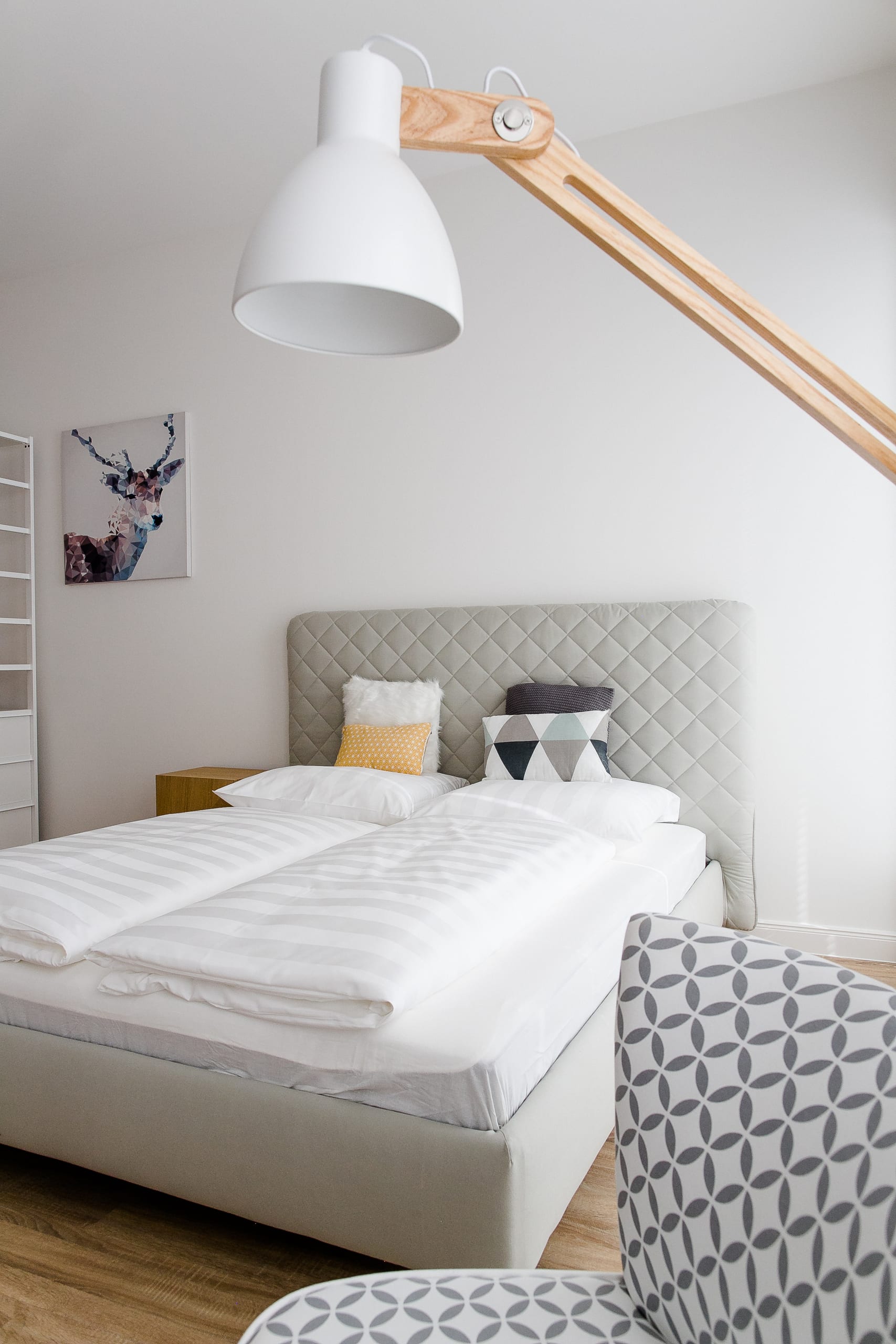 Schlafzimmer mit weißem Bett, gepolstertem Kopfteil, zwei Kissen und stehender Holzlampe