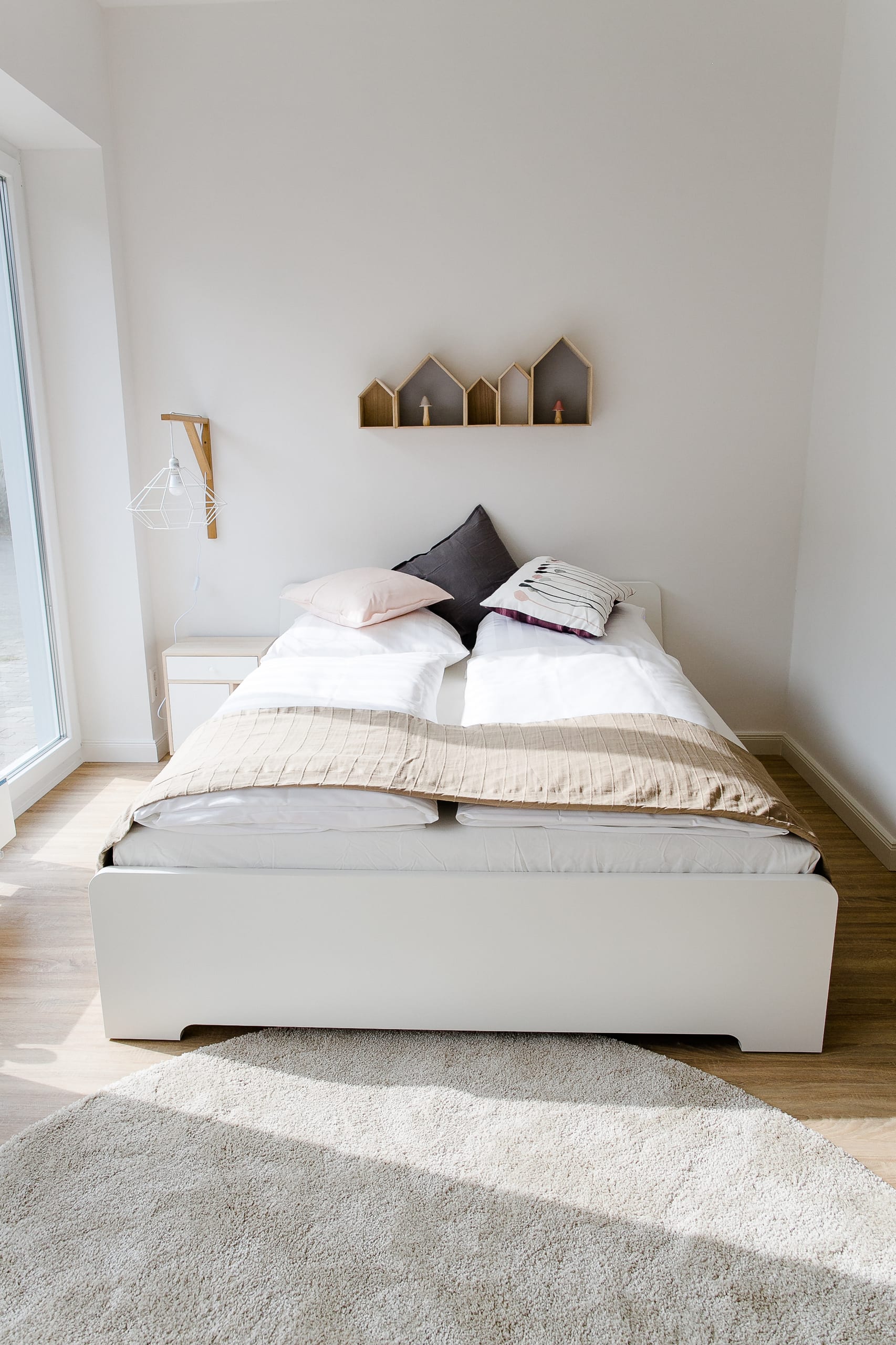 Schlafzimmer mit weißem Doppelbett, holzfarbenen Hausregalen und hellem Teppich