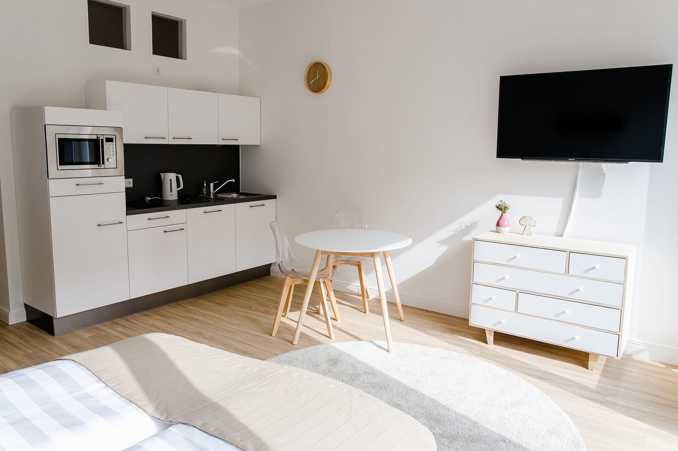 Heller Raum mit Küchenzeile, Esstisch, Fernseher und Kommode, Licht fällt durch Fenster