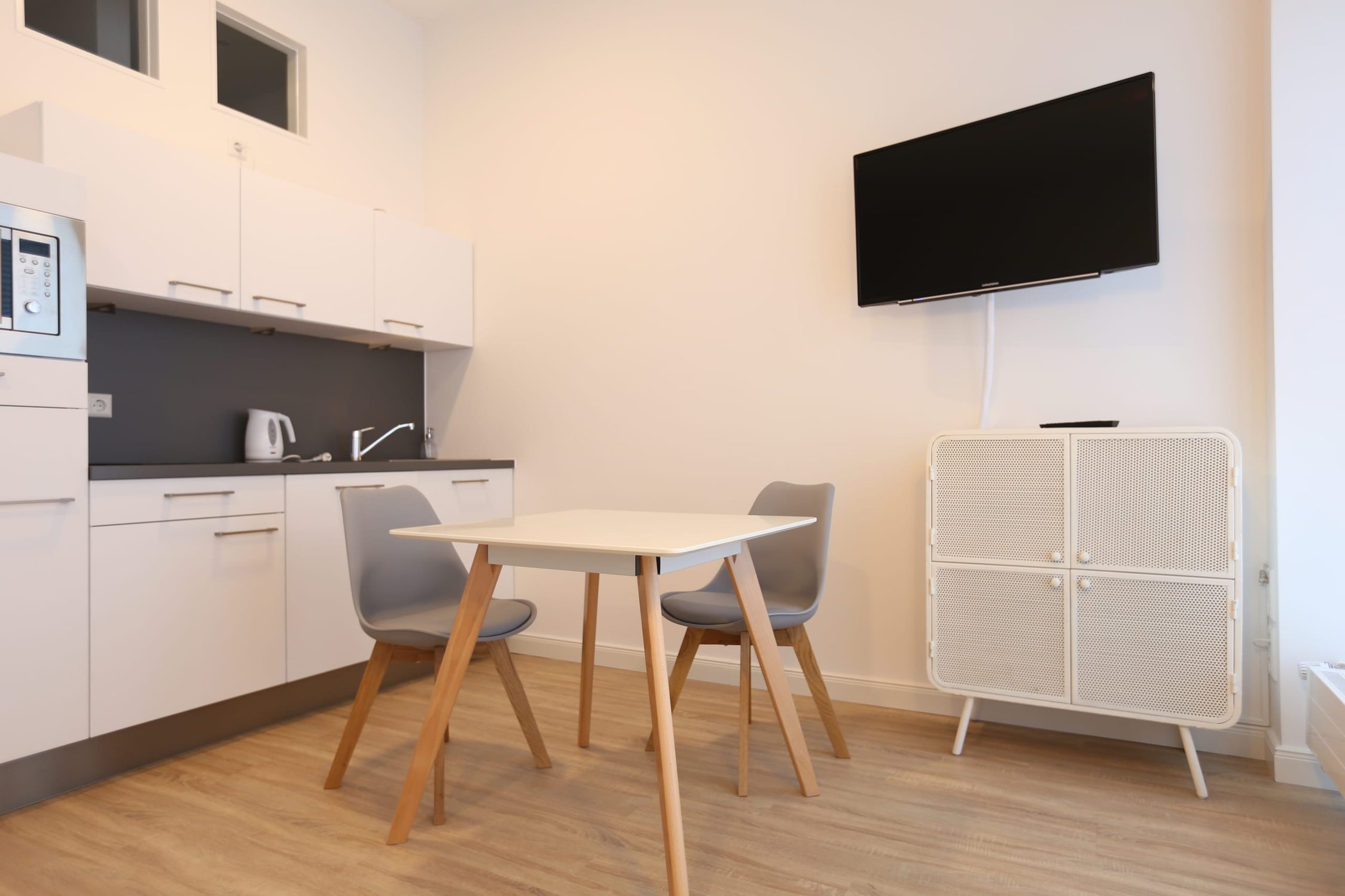 Helle Küchenzeile mit weißer Ablage, integriertem Mikrowellenherd, zwei Stühlen und Esstisch, warmes Licht