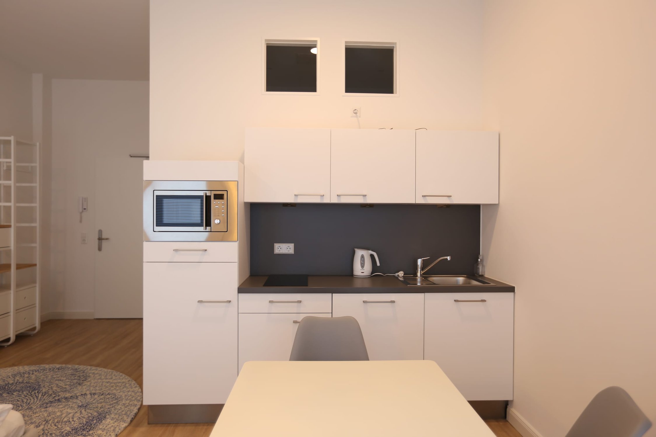 Küchenzeile mit weißer Mikrowelle, Spüle und Herdplatte vor dunkler Rückwand