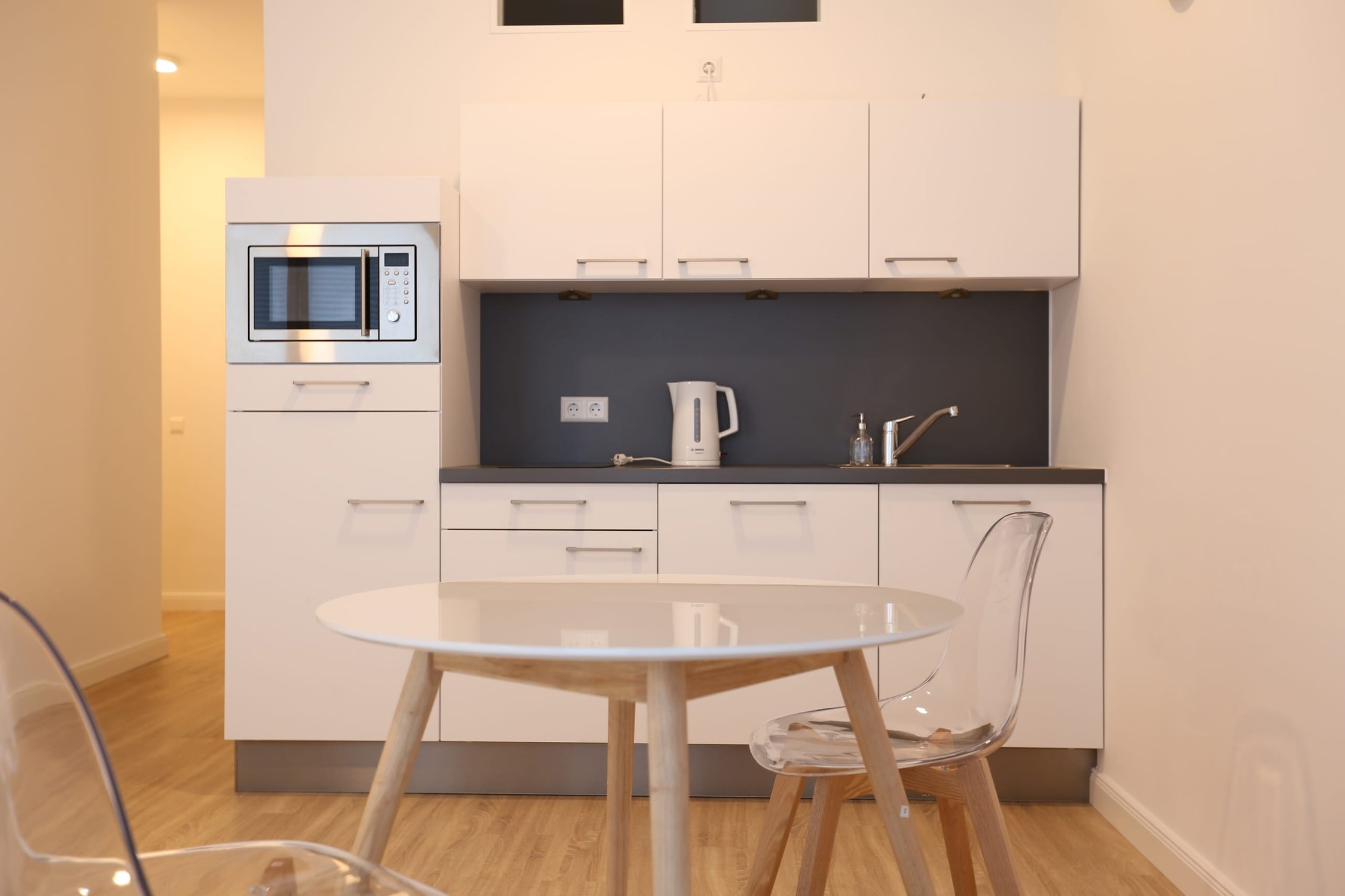 Helle Küchenzeile mit weißen Schränken, dunkler Arbeitsplatte und Esstisch mit zwei Stühlen