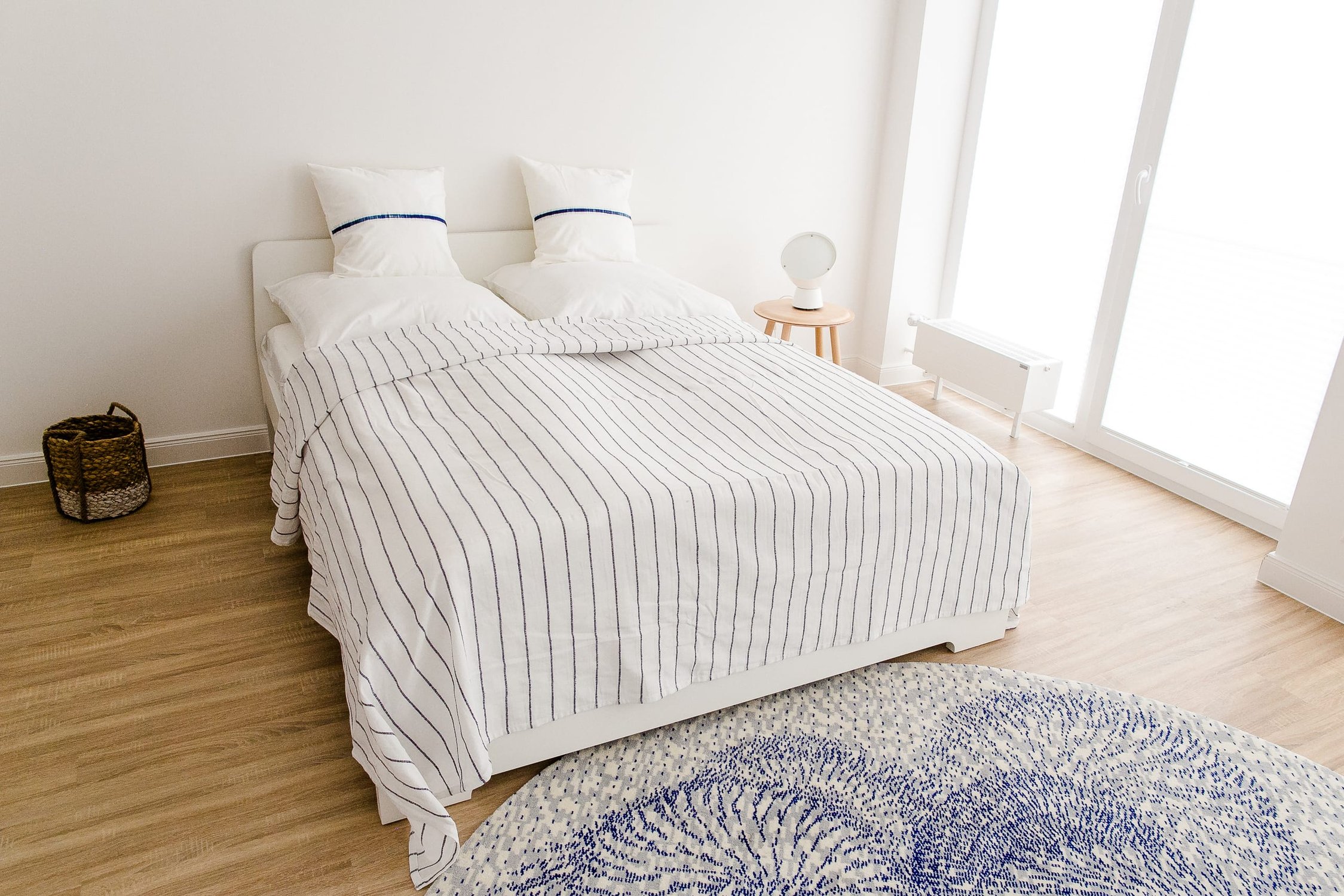 Schlafzimmer mit weißem Bett, gestreifter Bettwäsche, Holzfußboden und rundem Teppich