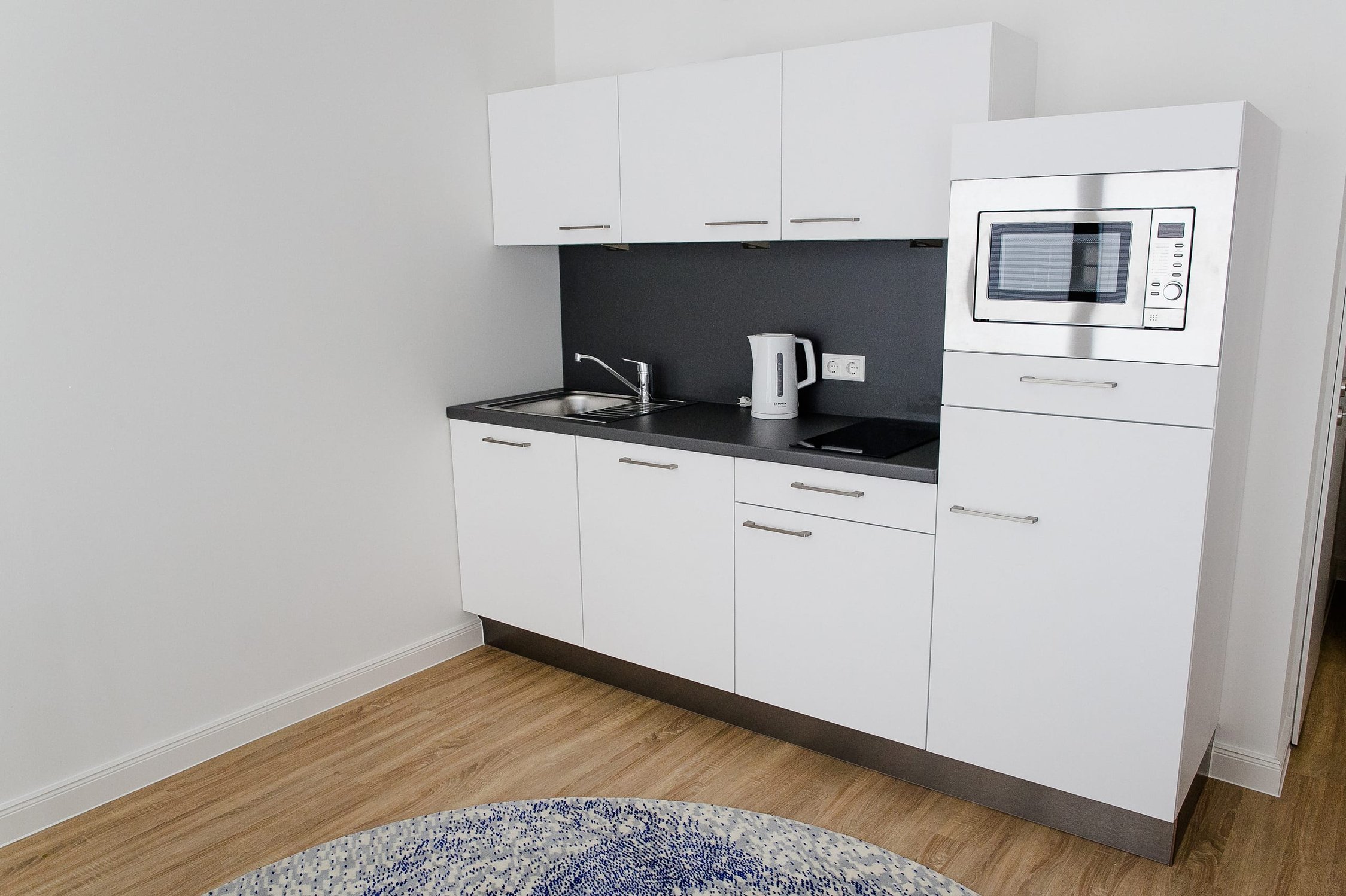 Kleine weiße Küchenzeile mit Spüle, Kochfeld, Wasserkocher und integrierter Mikrowelle