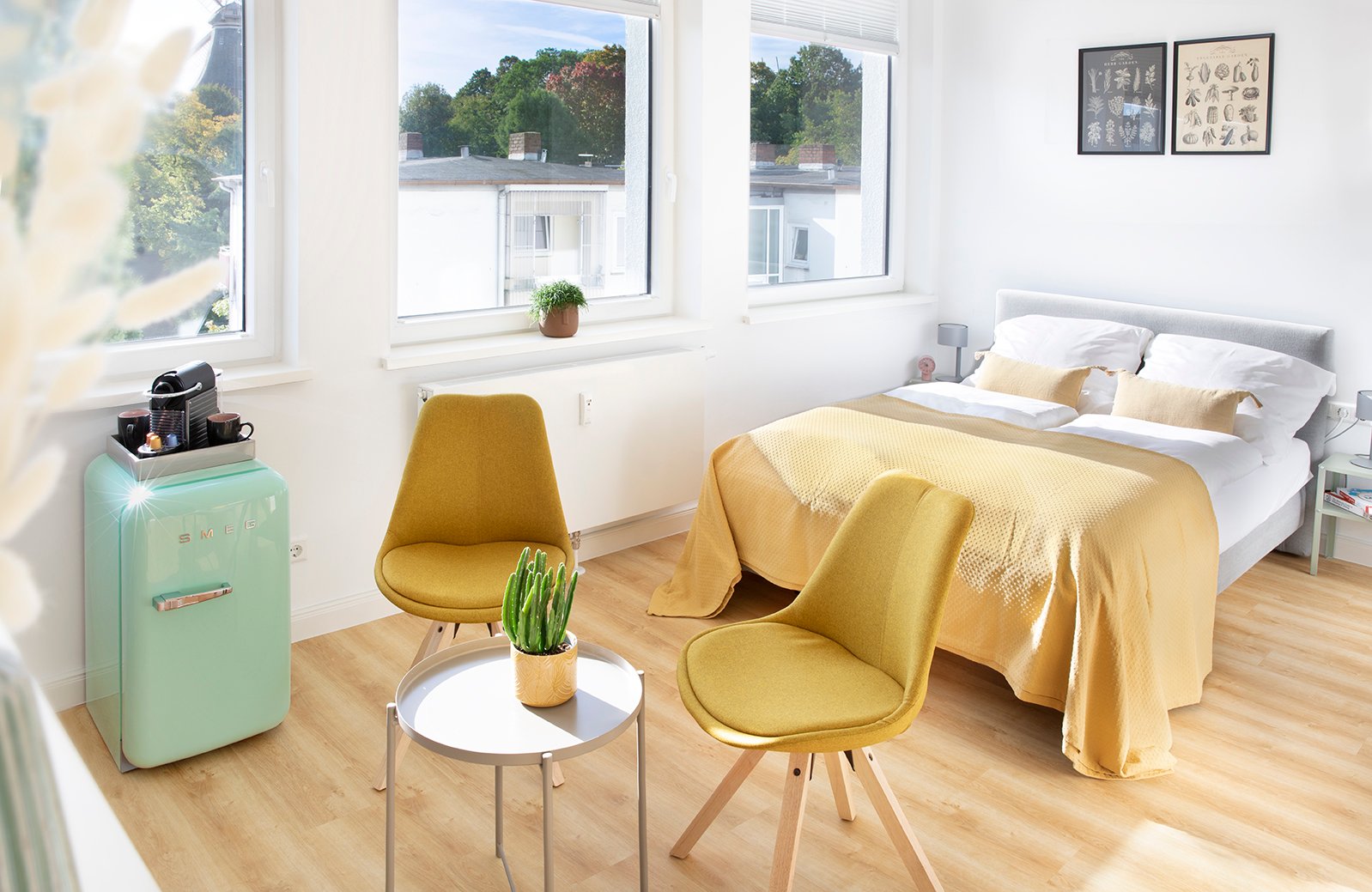Modernes Schlafzimmer mit Retro-Elementen. Gelbe Stühle, Vintage Mint-Kühlschrank, Doppelbett und großzügige Fenster. Stilvolles Design mit Holzboden.