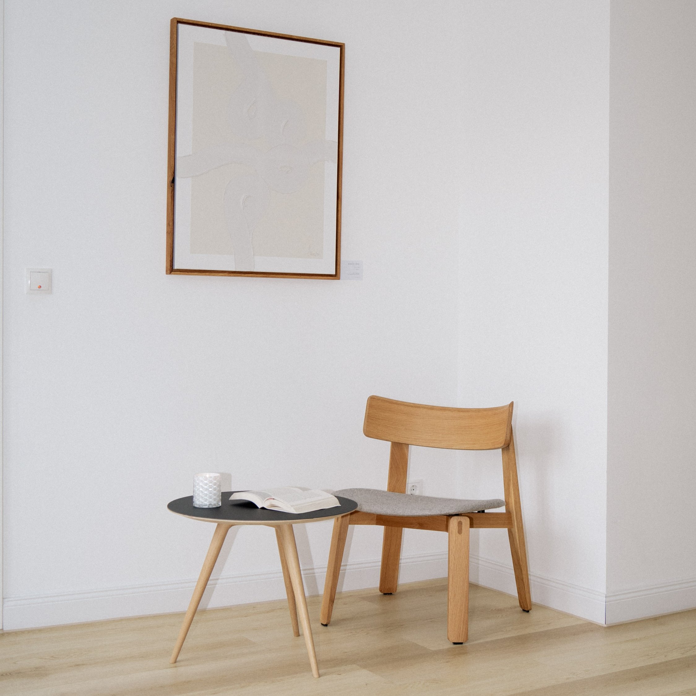 Minimalistischer Wohnraum mit Holzstuhl, schwarzem Beistelltisch und Spiegel. Skandinavisches Design mit natürlichen Materialien.