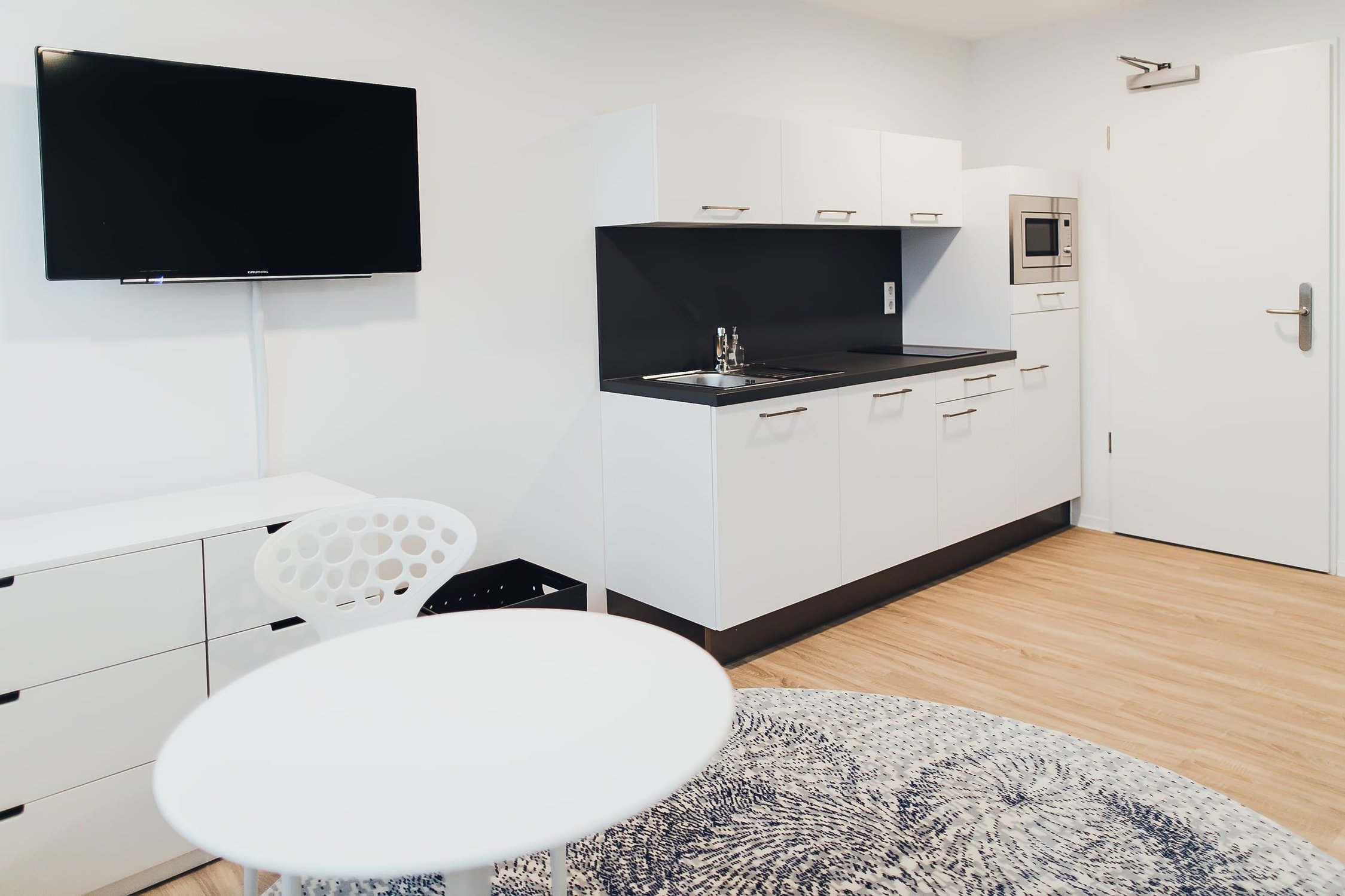 Apartment mit weißer Küchenzeile, Flatscreen, Schrank und hellem Holzboden