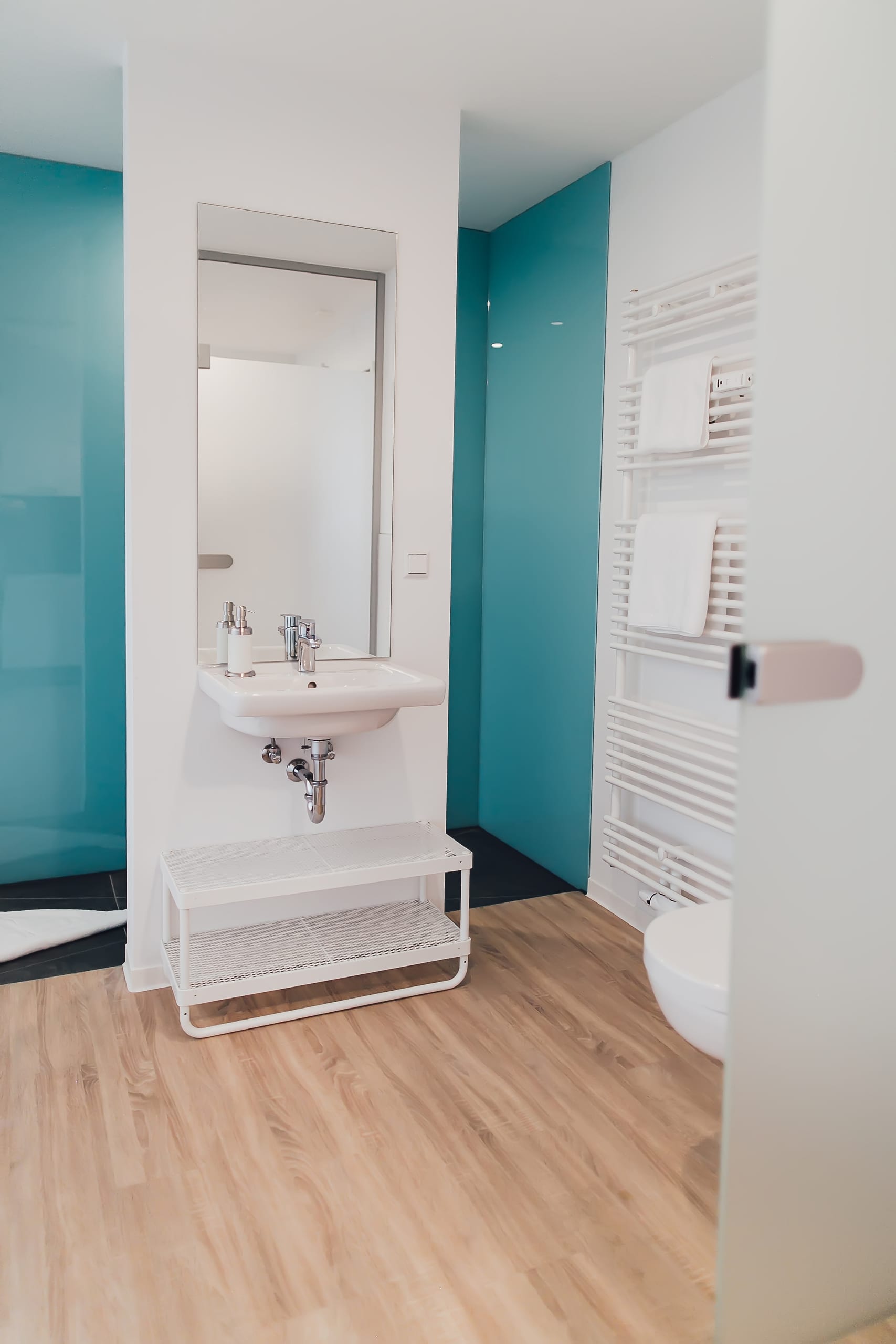 Modernes Badezimmer mit Holzboden, weißem Waschbecken, Spiegel und türkiser Wand