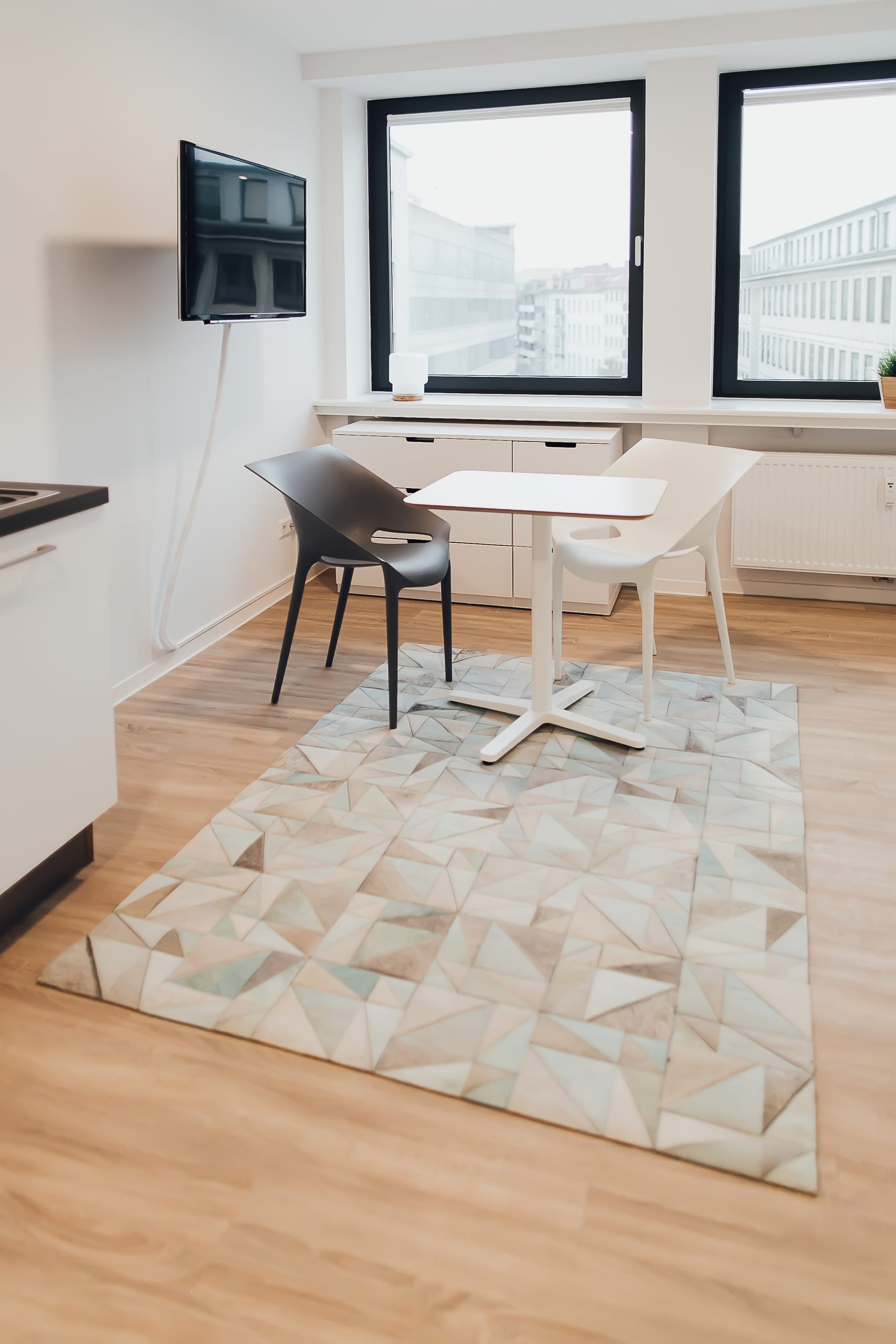 Heller Raum mit hellem Holzboden, geometrischem Teppich, zwei Stühlen und kleinem Tisch