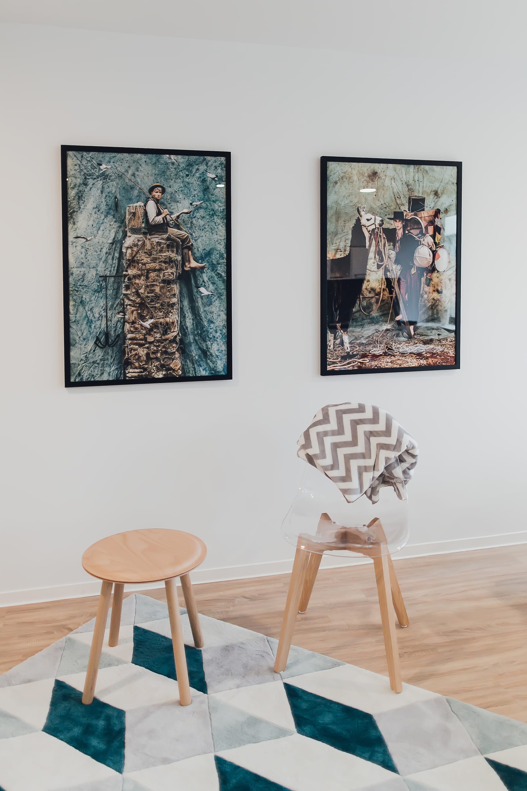 Zwei gerahmte Bilder an weißer Wand, Holzhocker, Transparenter Stuhl mit Decke, Geometrischer Teppich