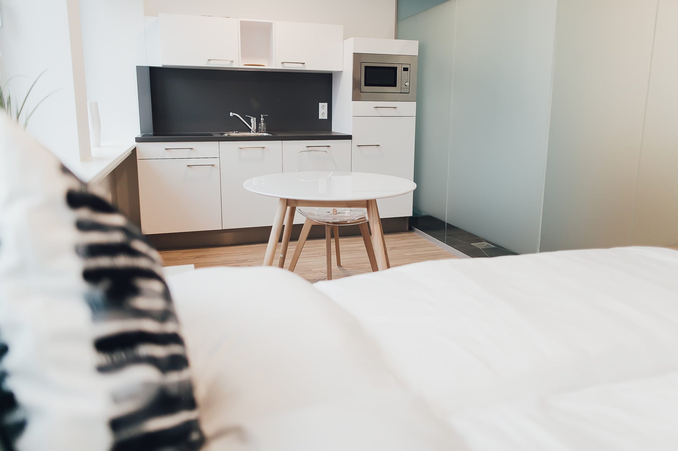 Kochnische mit weißen Schränken, dunkler Arbeitsplatte, rundem Esstisch, durch eine Glaswand abgetrennt