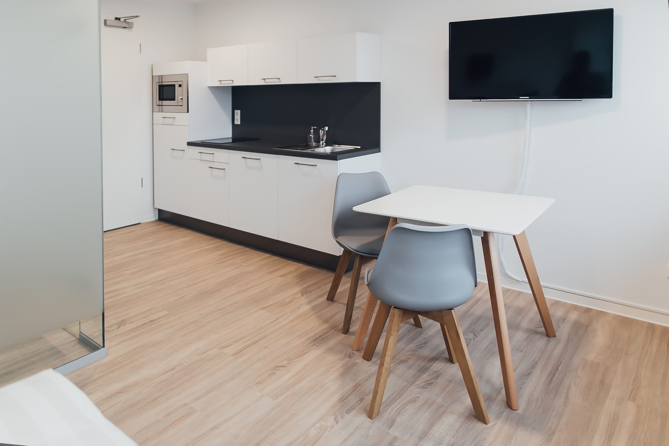 Moderne Küchenzeile mit Mikrowelle, Dunstabzugshaube, Tisch und Stühlen auf Holzfußboden