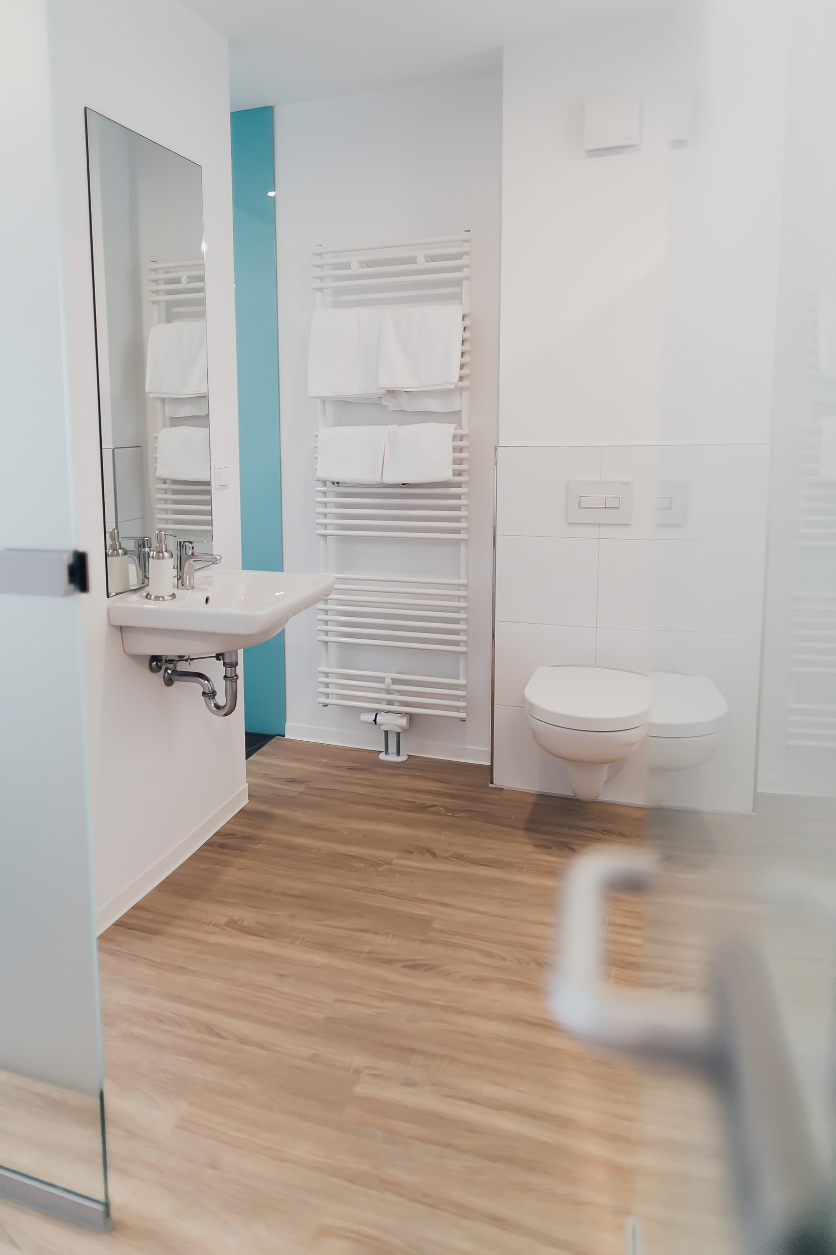 Badezimmer mit Holzoptik-Boden, weißem Waschbecken, Heizkörper und Toilette