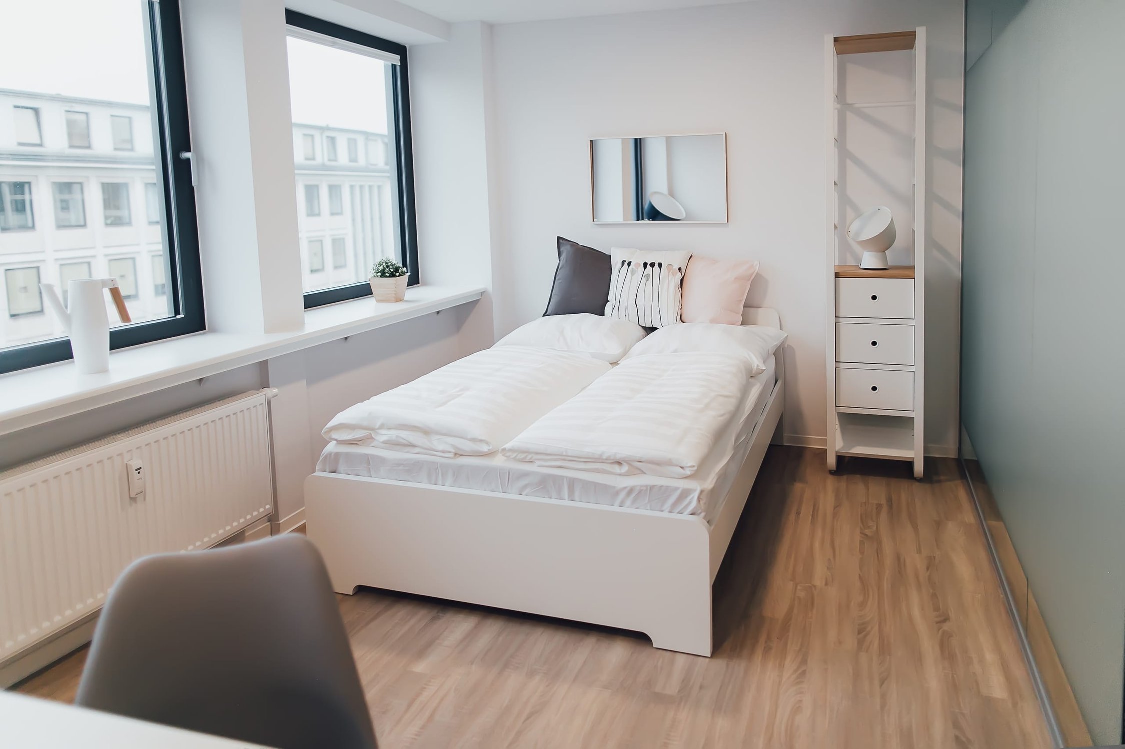 Helles Schlafzimmer mit Einzelbett, Fenster und Regal mit drei Schubladen