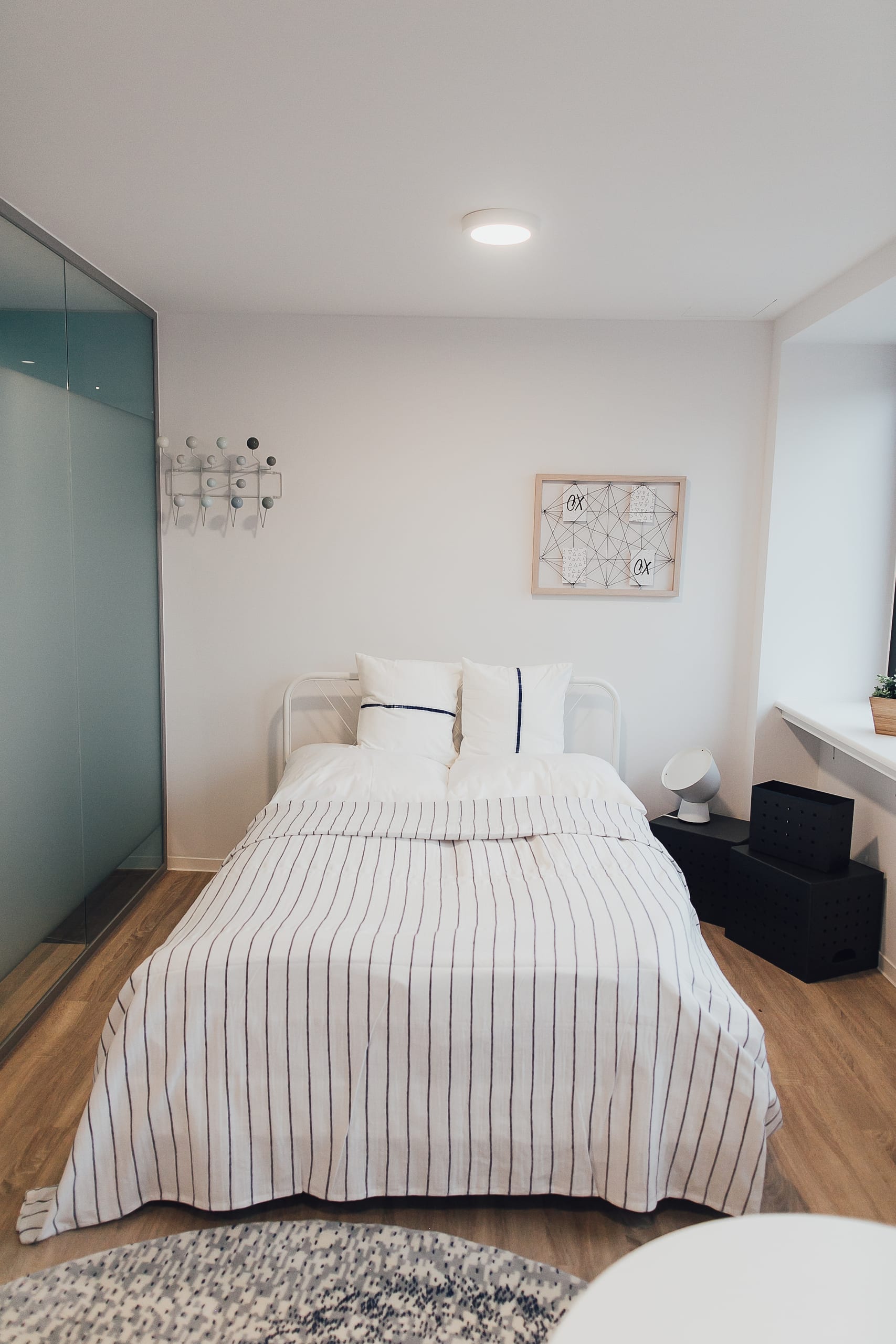 Schlafzimmer mit weiß gestreiftem Bett, Holzfußboden und kleiner runder Teppich