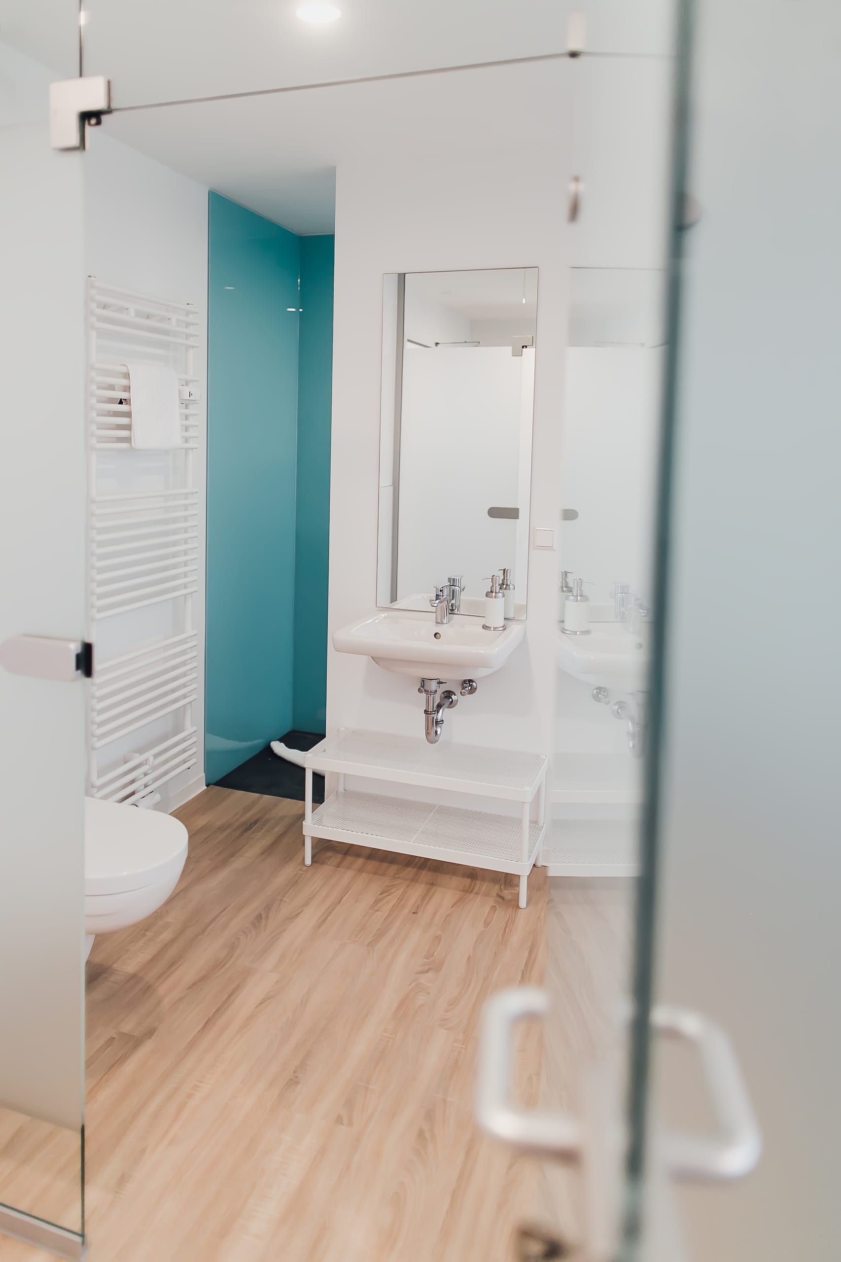 Modernes Badezimmer mit hellem Holzboden, weissen Wänden und türkisem Akzentbereich