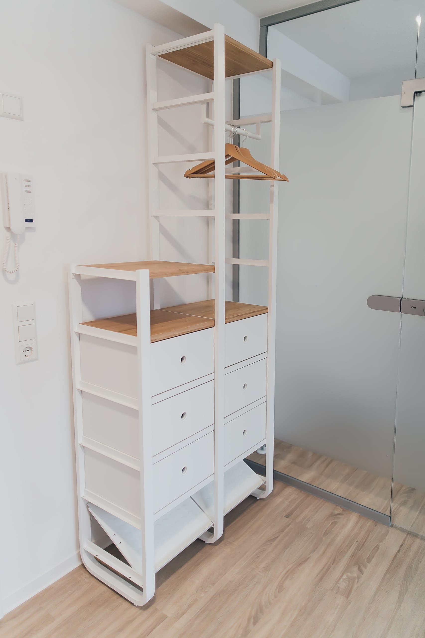 Offenes Kleiderregal mit Holzbrettern, weißen Schubladen und Kleiderbügel daneben
