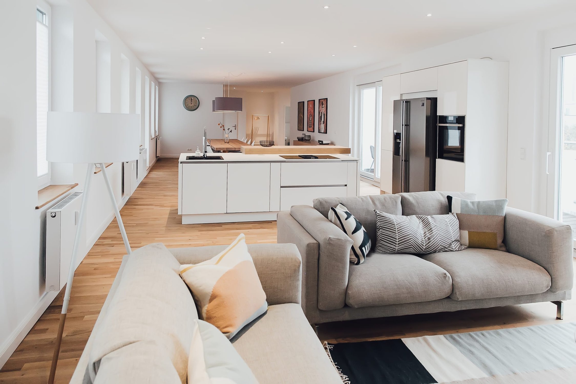Heller Wohnraum mit zwei grauen Sofas, weißer Küche und Esstisch, Holzboden