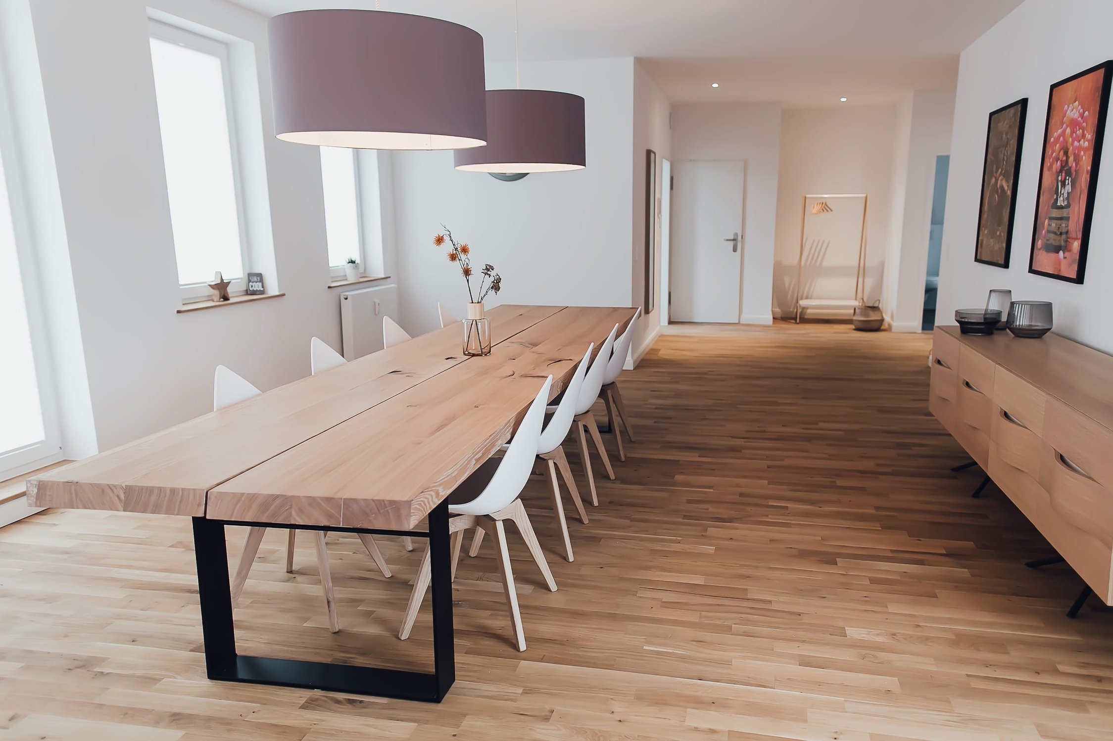 Heller Essbereich mit langem Holztisch für zehn Personen, zwei grauen Hängelampen, Holzboden