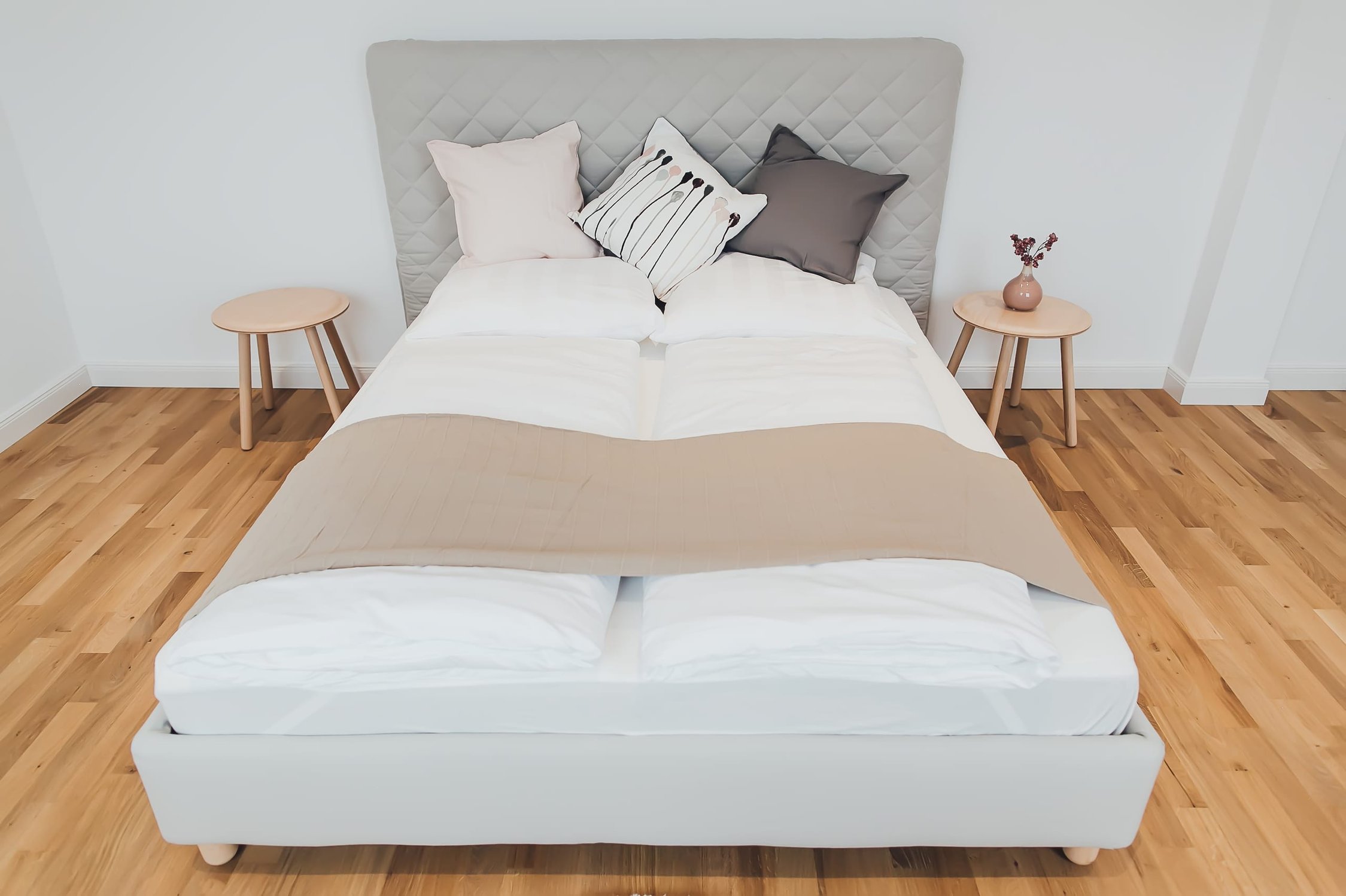 Schlafzimmer mit Doppelbett, weißer Bettwäsche, Steppkopfteil und heller Holzboden