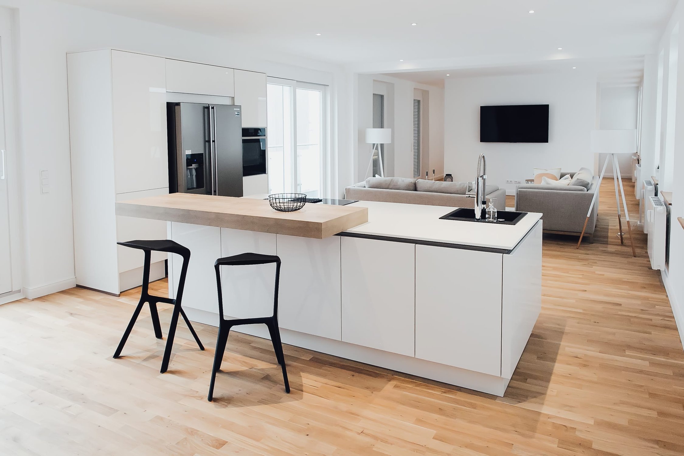 Moderne offene Küche mit Kochinsel, schwarzen Hockern und Holzfußboden, im Hintergrund Wohnbereich