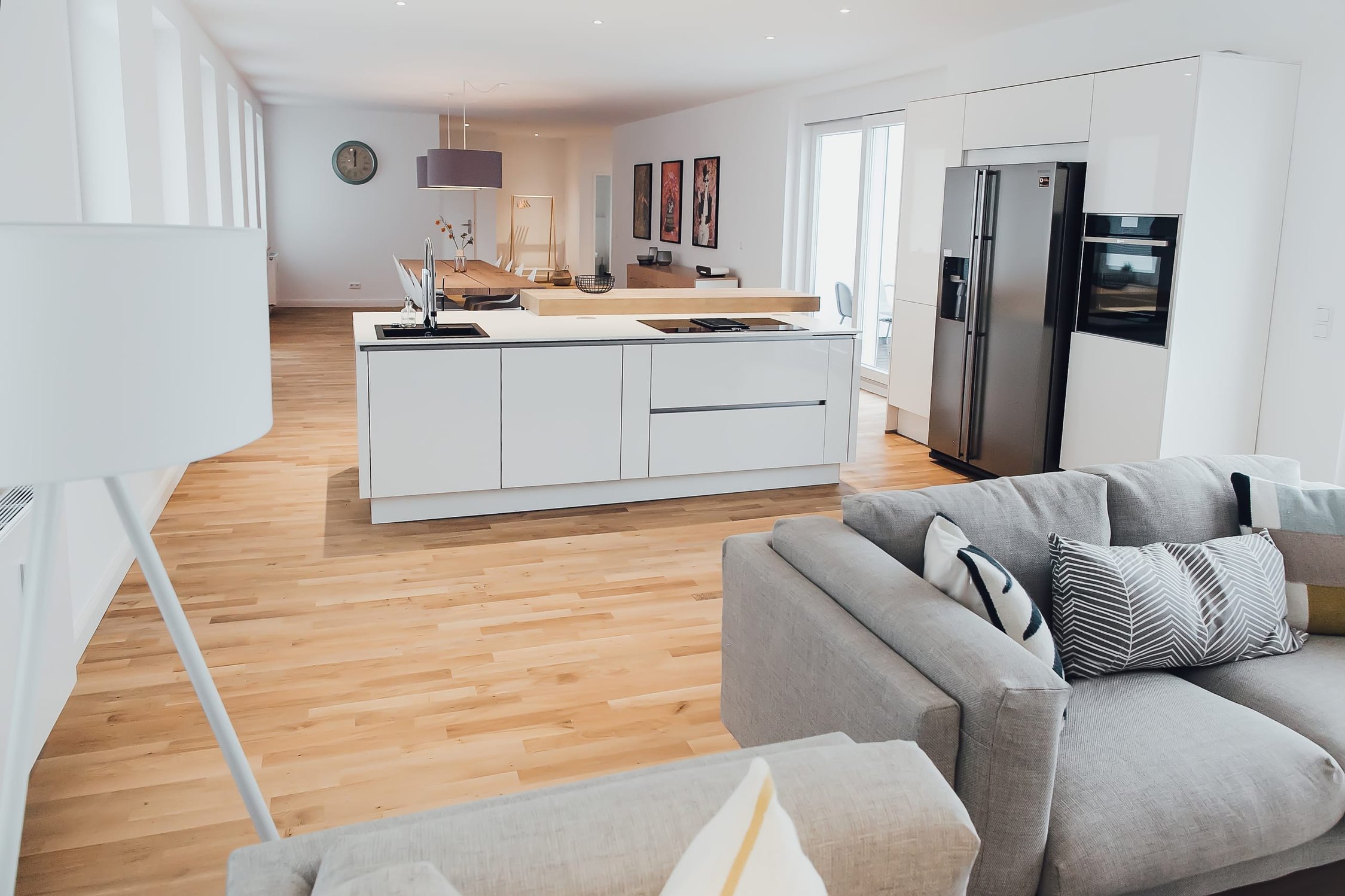 Offener Wohnbereich mit grauer Couch, weißer Küche und hellem Holzfußboden