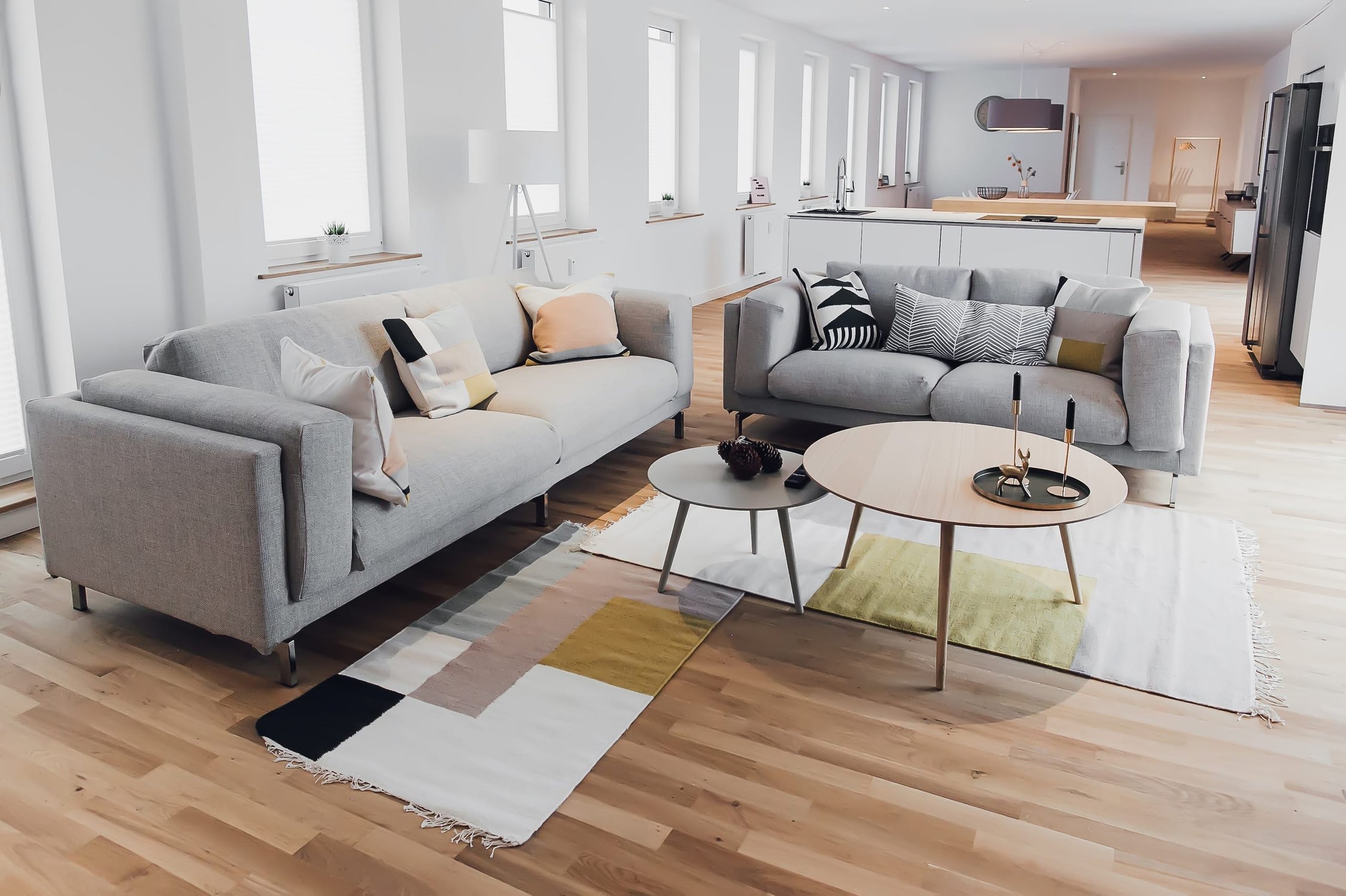 Helles Wohnzimmer mit zwei grauen Sofas, runden Couchtischen und geometrischem Teppich