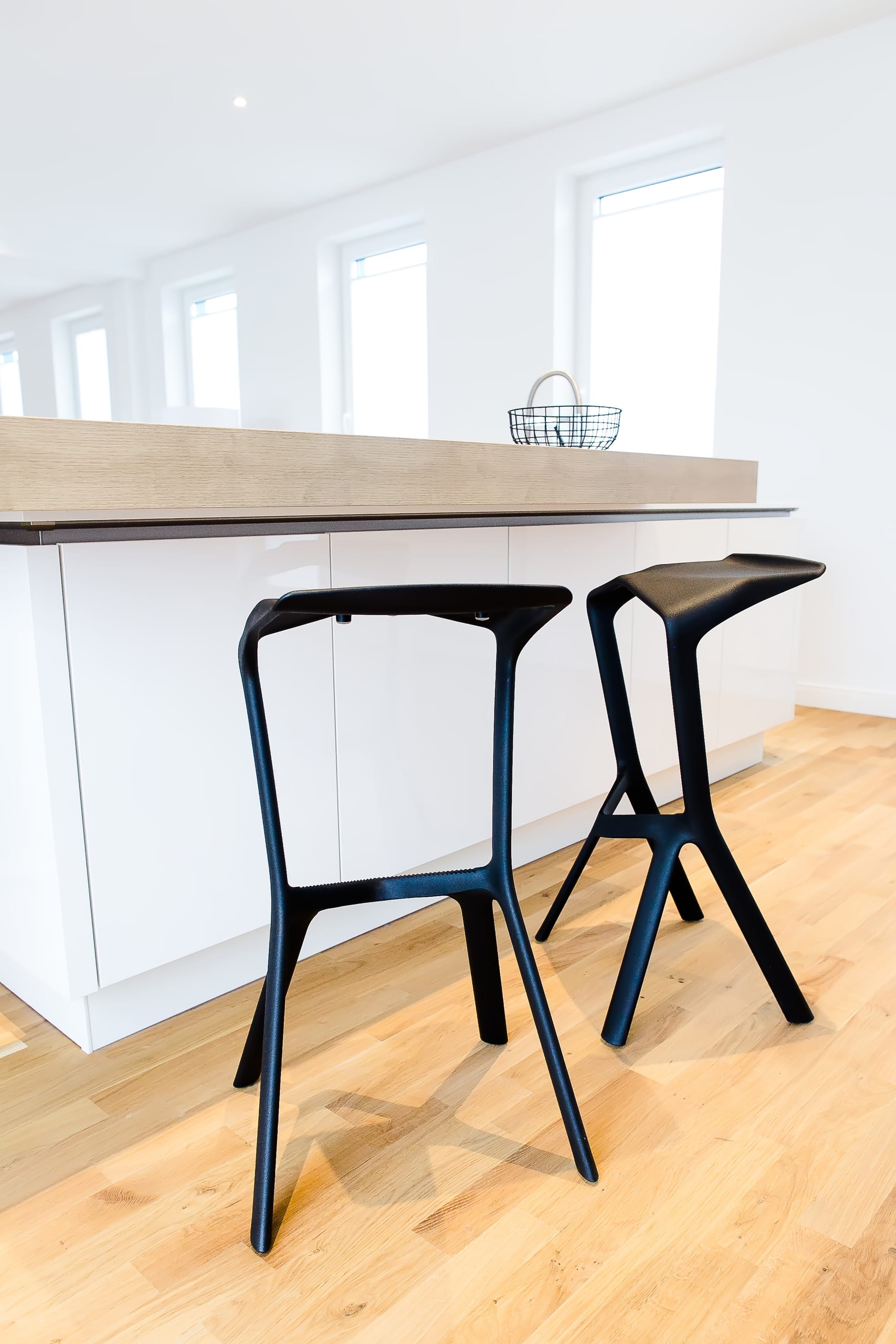 Zwei schwarze Barhocker an einer Kücheninsel in hellem Raum, Holzoptikboden