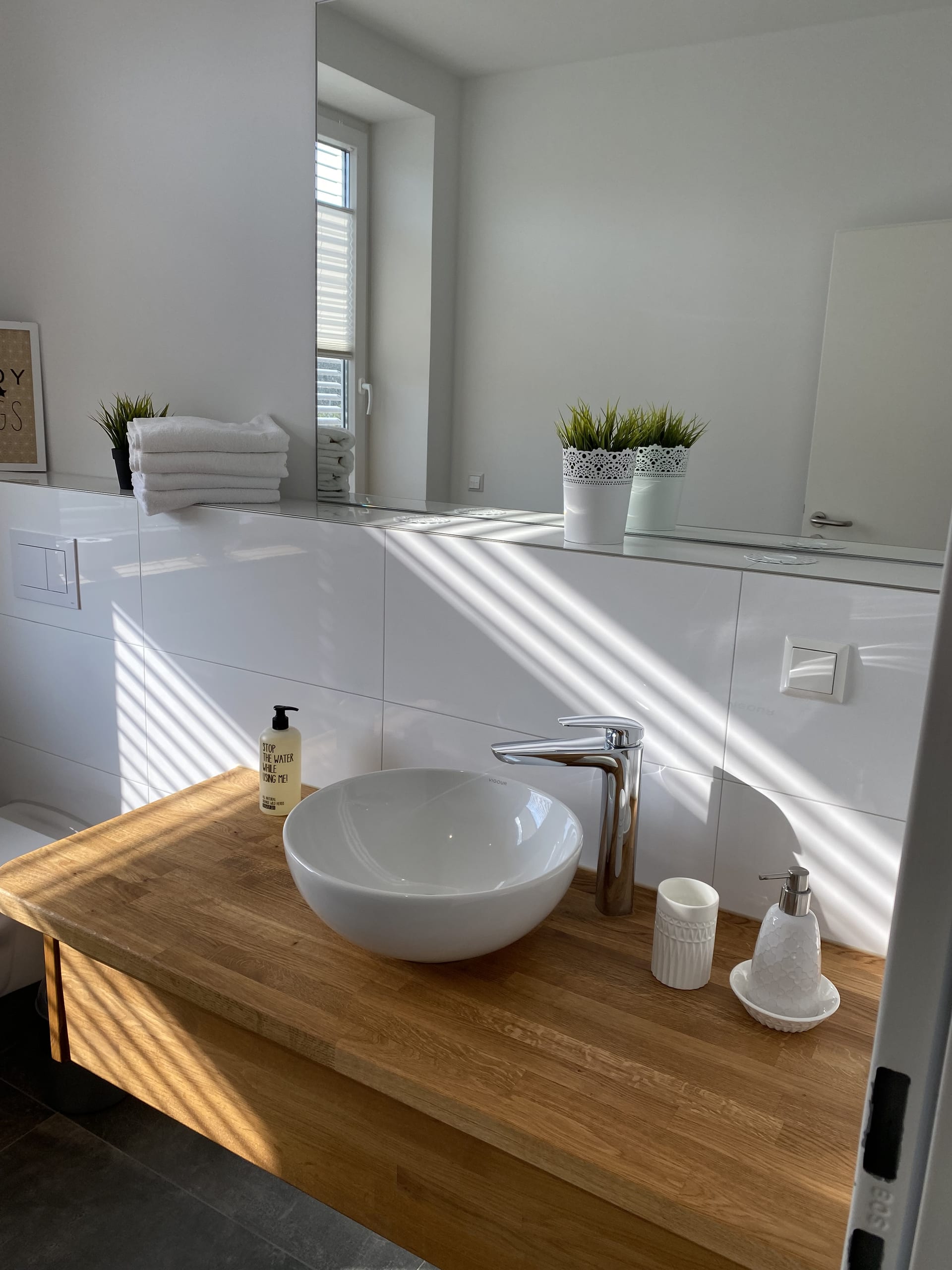 Badezimmer mit weißem Aufsatzwaschbecken, poliertem Wasserhahn und Holzwaschtisch mit Sonnenstreifen